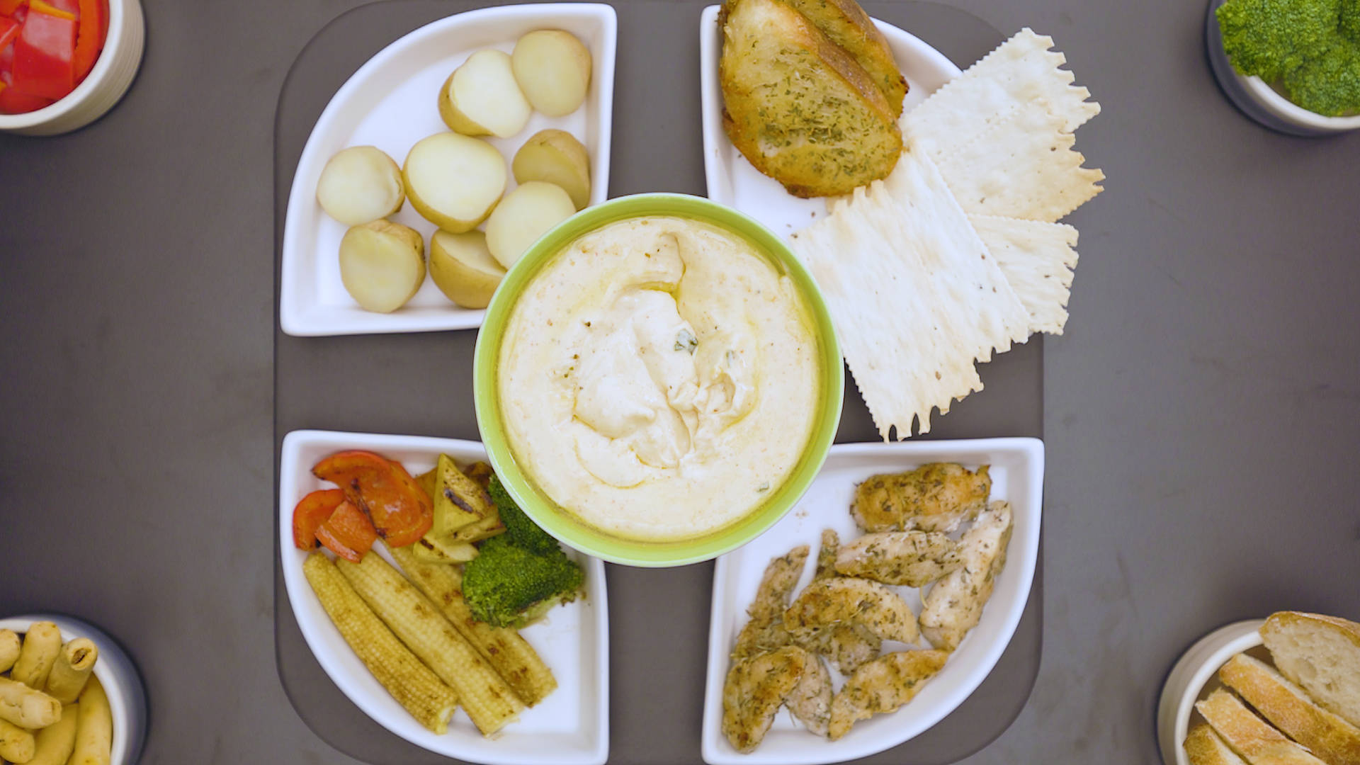 Cheese 桌布 壁紙 — 俯瞰一個奶油鷹嘴豆泥碗，周圍有各種蘸料，包括馬鈴薯、麵包脆片、雞肉和蔬菜，放在灰色托盤上。
