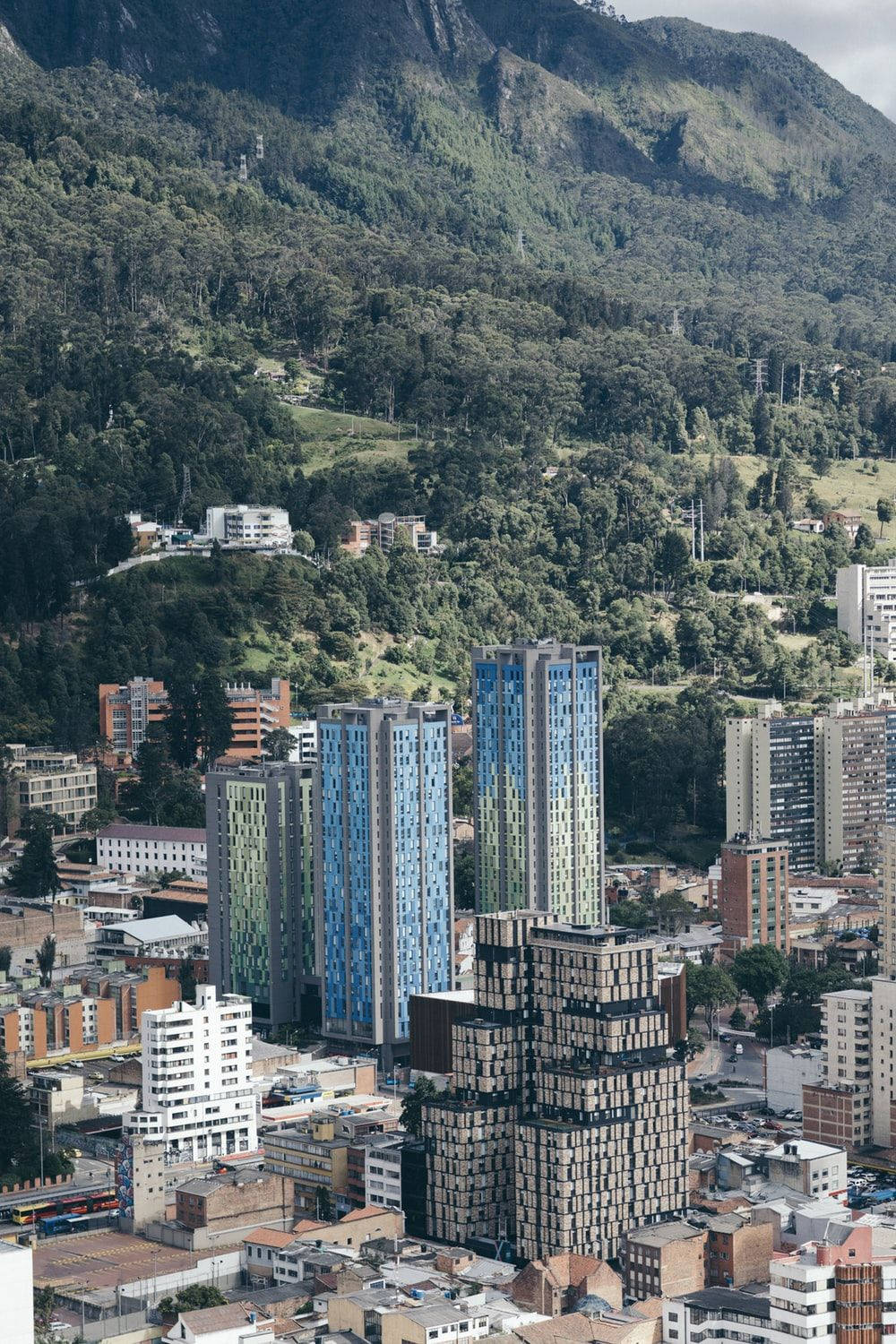 Bogota 桌布 壁紙 — 俯瞰一個密集城市，坐落於翠綠山谷中，現代高樓聳立於舊建築之間。