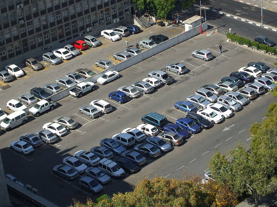 汽車 桌布 壁紙 — 俯瞰一個擁擠的城市停車場，車輛整齊地排列在建築物和樹木旁邊。