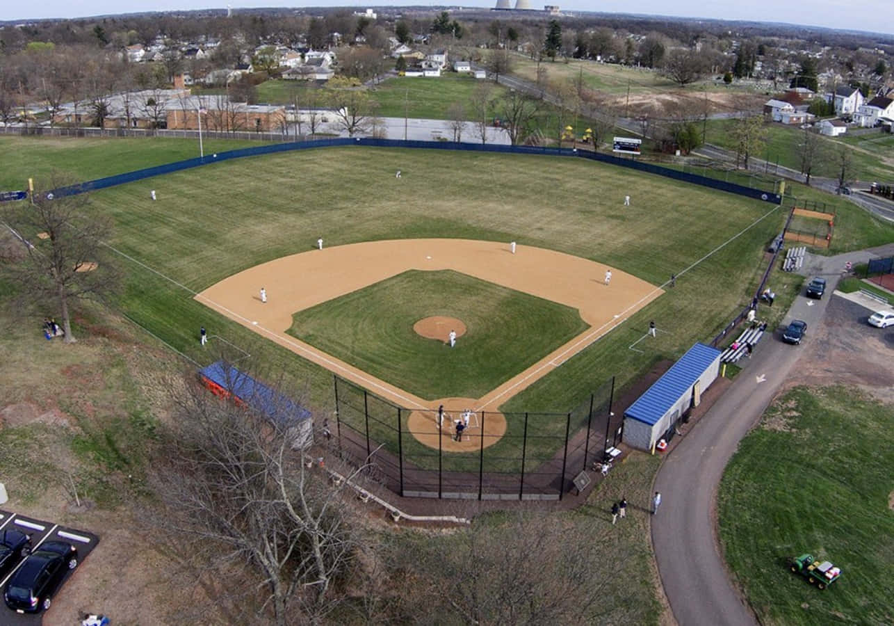Baseball Field 桌布 壁紙 — 俯瞰一個棒球場，球員正在比賽，周圍是郊區房屋和光禿禿的樹木。