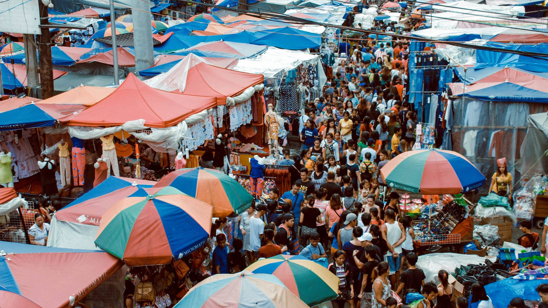Umbrella 桌布 壁紙 — 俯瞰一個熙熙攘攘的戶外市場，色彩繽紛的雨傘和擁擠的攤位在明亮的日光下。