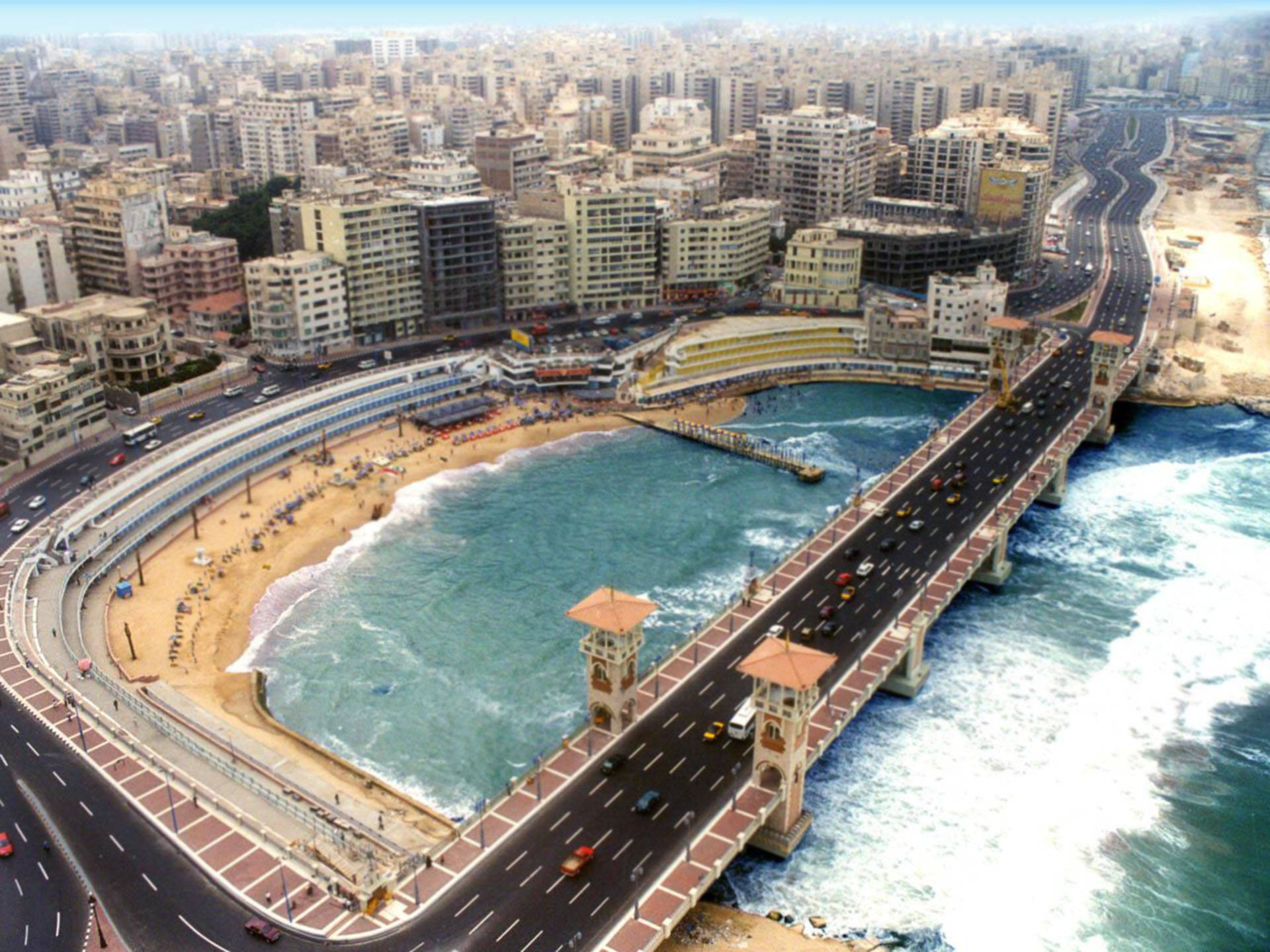Alexandria 桌布 壁紙 — 俯瞰一個繁華的海濱城市，擁有彎曲的海灘和一座橫跨波濤洶湧海洋的橋樑。