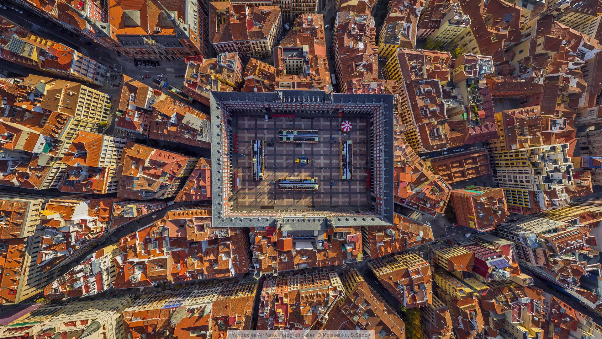 Madrid 桌布 壁紙 — 俯瞰一個陽光普照的歐洲城市廣場，周圍是密集的橙色瓦片屋頂和狹窄的街道。