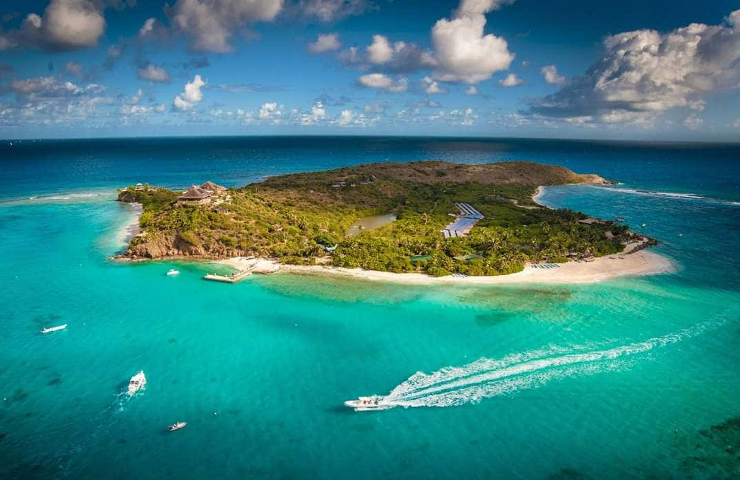 Caribbean Island 桌布 壁紙 — 俯瞰一個鬱鬱蔥蔥的熱帶島嶼，擁有碧綠的海水和點綴著船隻的白色沙灘。
