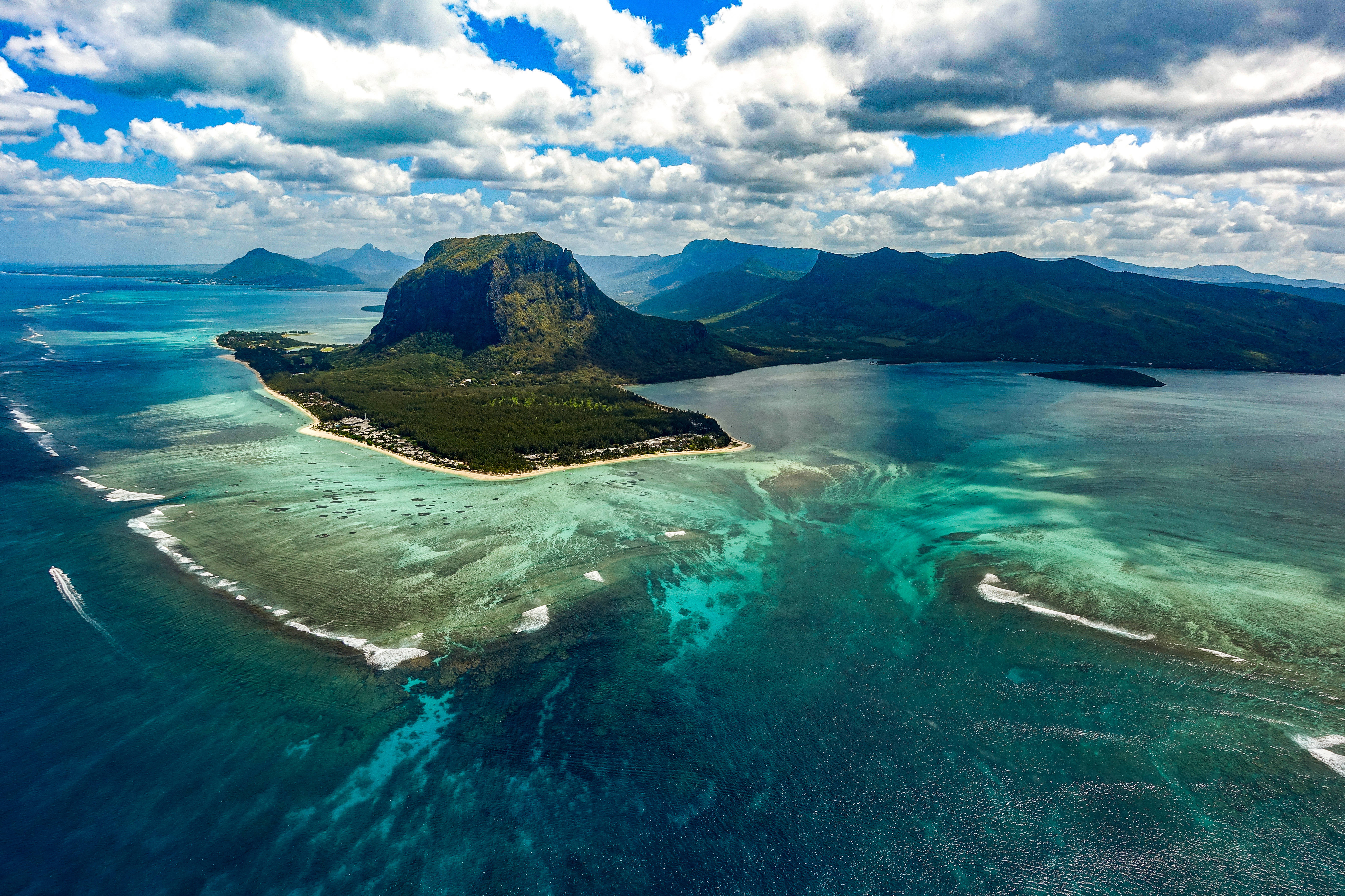 Mauritius 桌布 壁紙 — 俯瞰一個鬱鬱蔥蔥的綠色島嶼，島上有一座高聳的山峰，周圍環繞著充滿活力的碧綠海水和白色沙灘，天空部分多雲。
