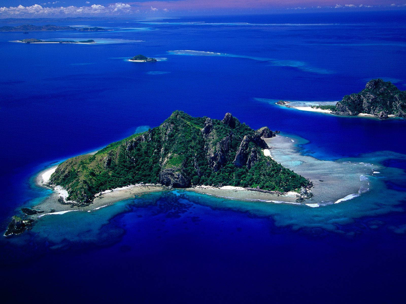 Fiji 桌布 壁紙 — 俯瞰一個鬱鬱蔥蔥的綠色島嶼，擁有白色沙灘，被深藍色海洋和珊瑚礁環繞。