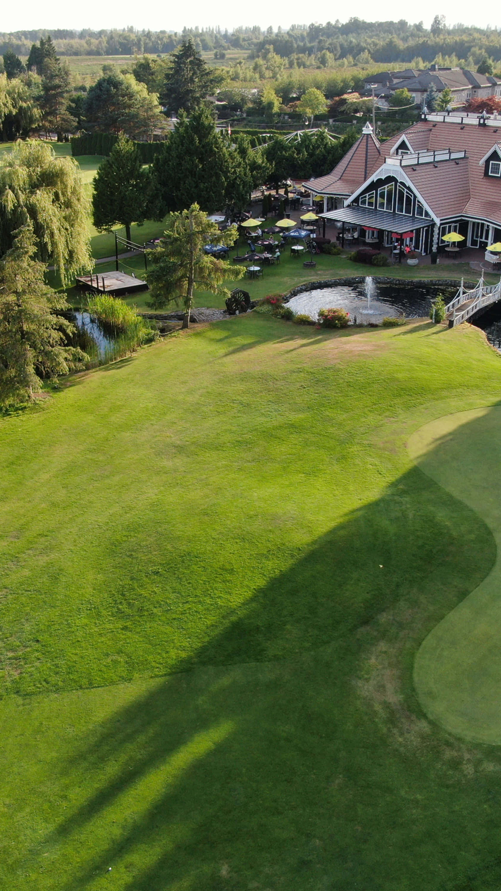 Golf Green 桌布 壁紙 — 俯瞰一個鬱鬱蔥蔥的高爾夫球場，會所和噴泉沐浴在金色的晨光中。