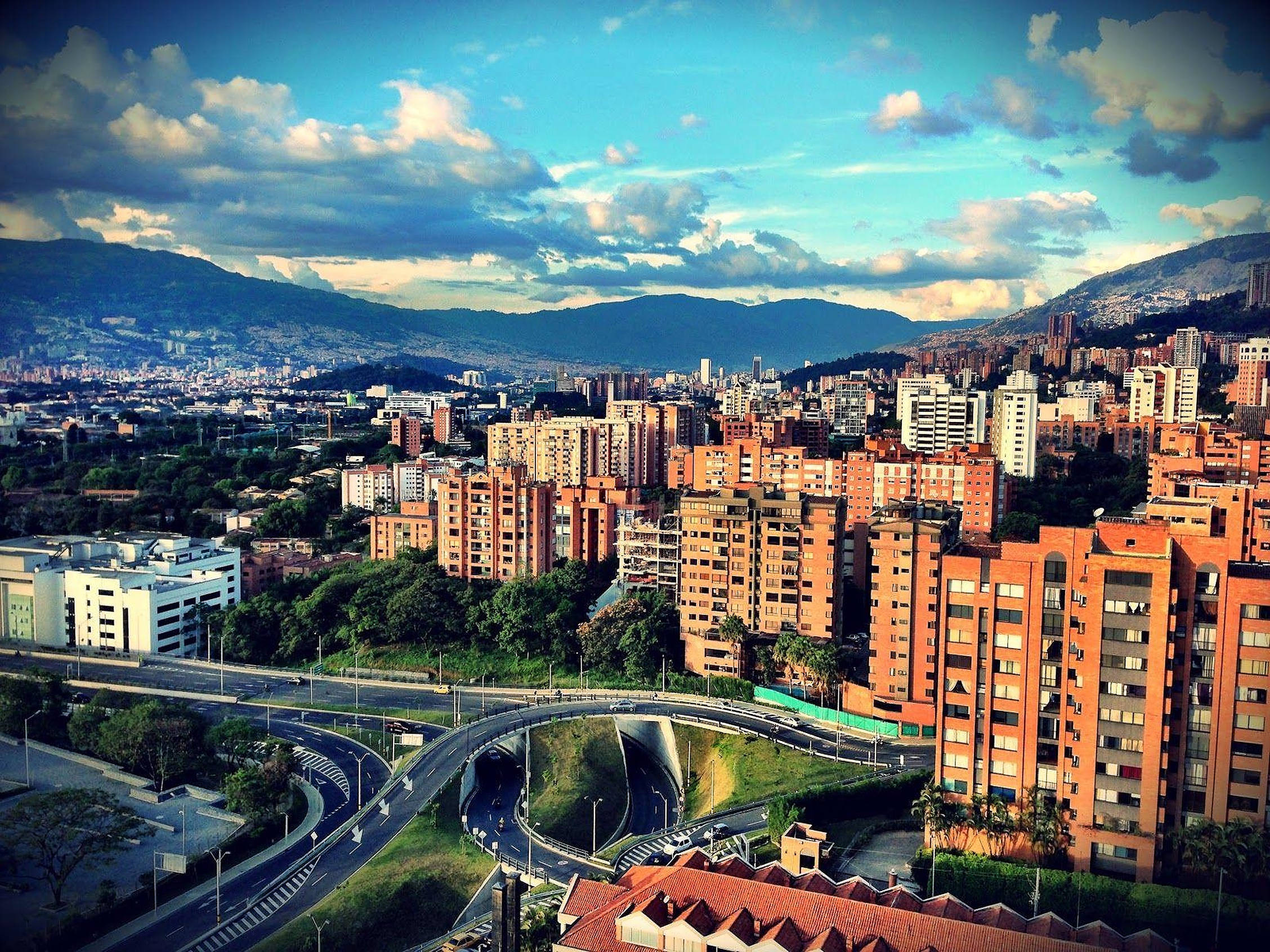 Colombia 桌布 壁紙 — 俯瞰一座坐落於翠綠山丘之間、在戲劇性藍天白雲下的廣闊城市。
