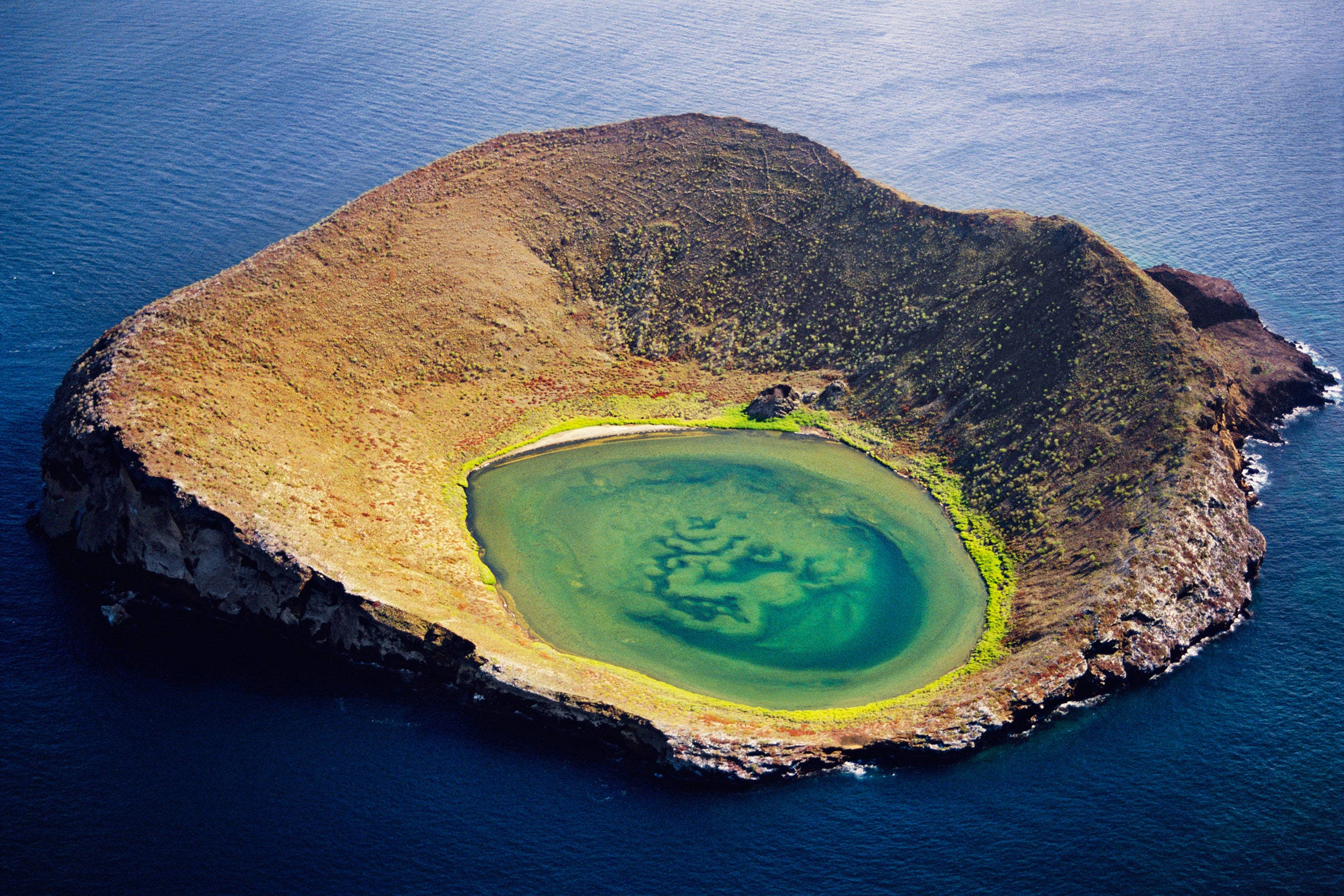 South America 桌布 壁紙 — 俯瞰一座火山島，島上有一個碧綠色的潟湖，坐落於崎嶇的火山口內，四周是深藍色的海洋。