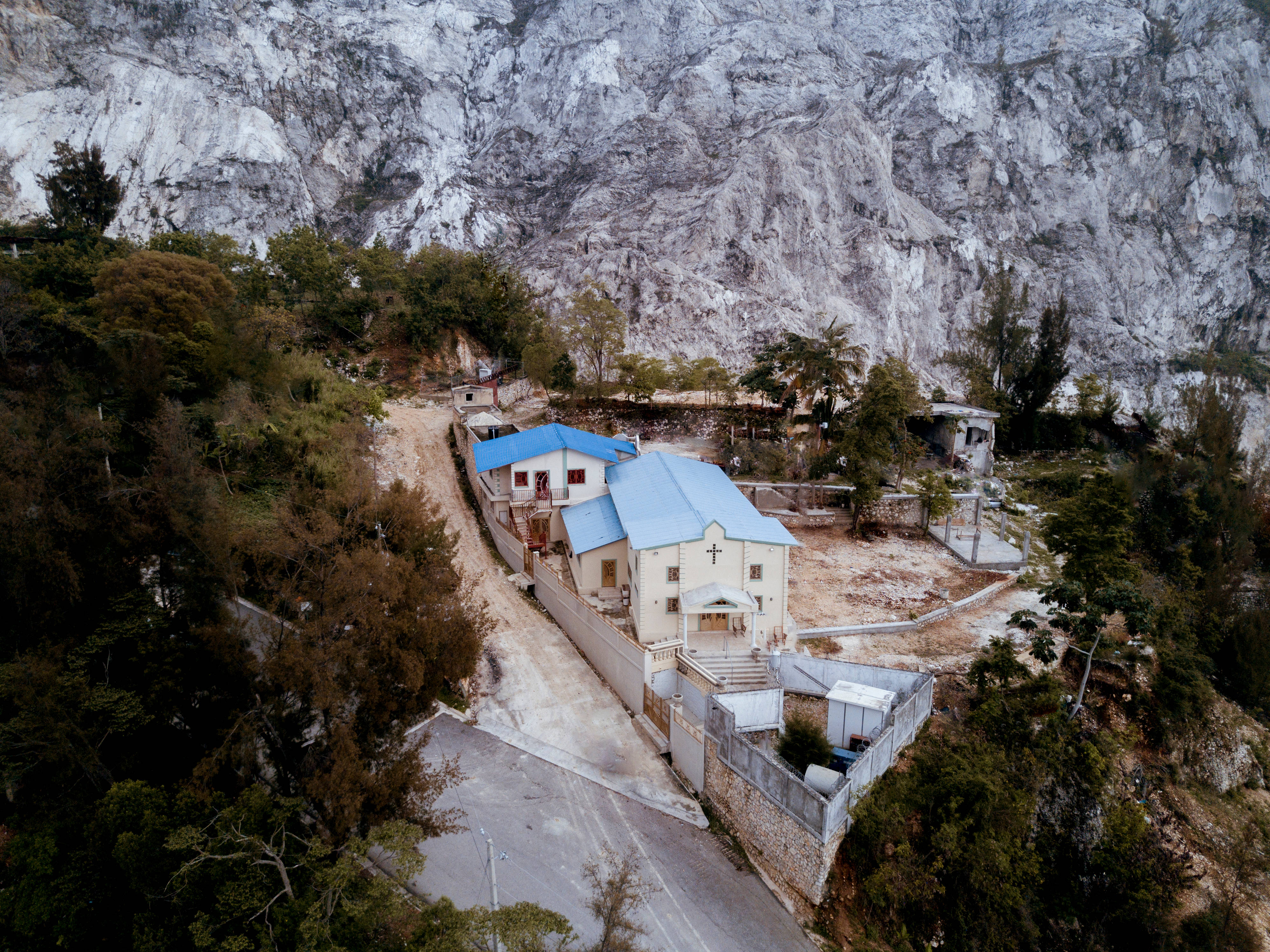 Haiti 桌布 壁紙 — 俯瞰一座藍色屋頂的小白色教堂，坐落在森林山谷中，背靠高聳的岩石峭壁。