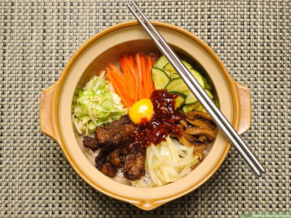 烹飪 桌布 壁紙 — 俯瞰一碗冒煙的韓國石鍋拌飯，上面有色彩繽紛的蔬菜、肉類和生蛋黃，並以筷子點綴。