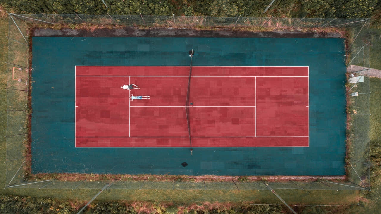 720p Tennis 桌布 壁紙 — 俯瞰兩人在被綠植環繞的紅藍綠色網球場上休息的景象。