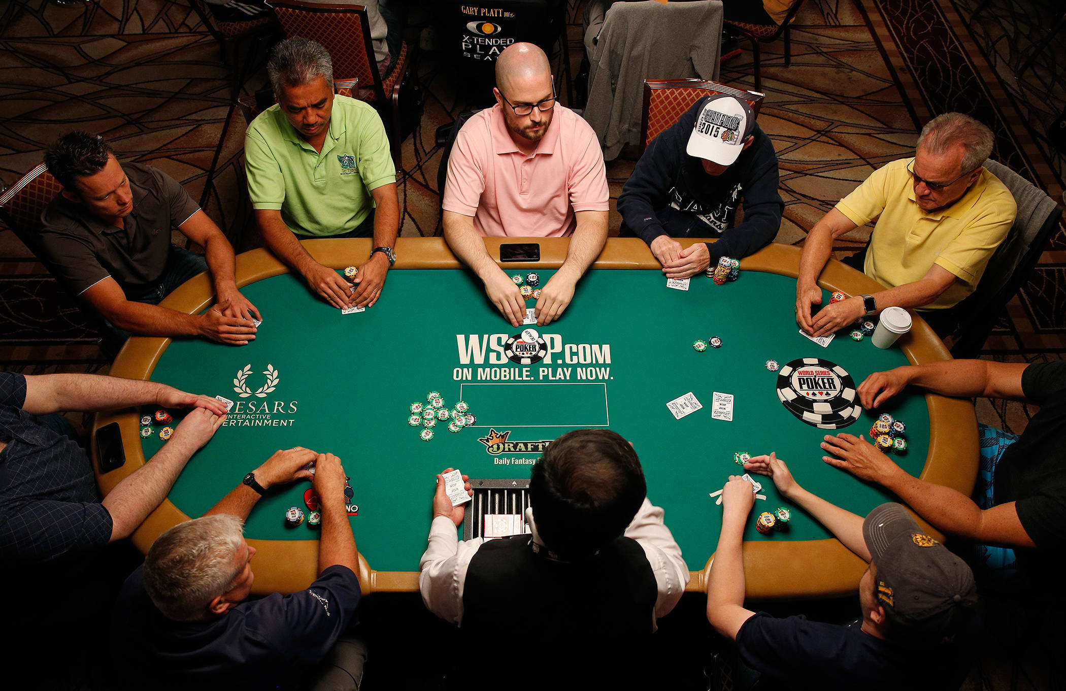Poker 桌布 壁紙 — 俯瞰八名男子在昏暗賭場房間的綠色撲克桌上專注地玩牌。