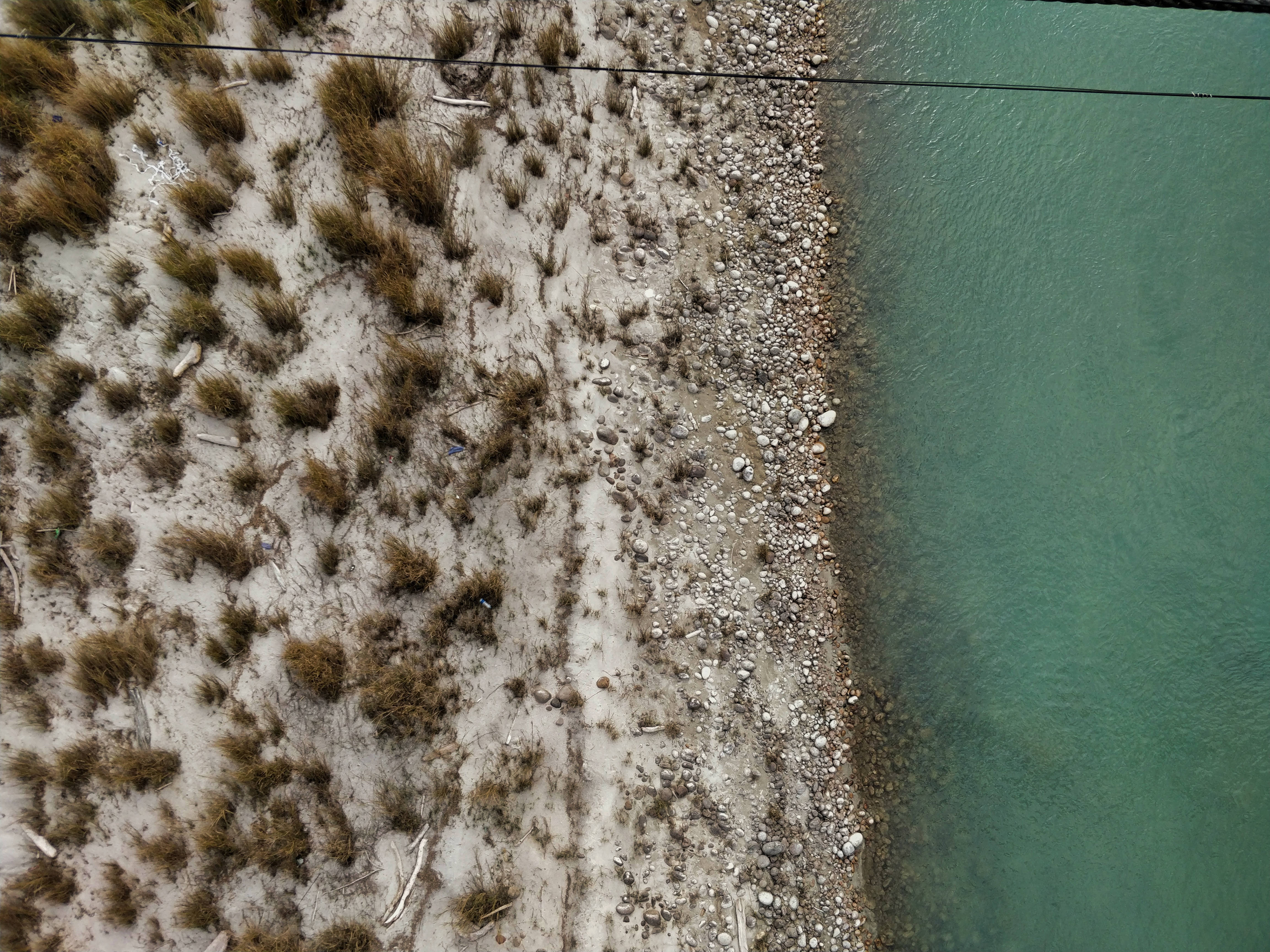 不丹 桌布 壁紙 — 俯瞰圖：碧綠河流與沙岸交匯，岸邊有乾草和散落的岩石。