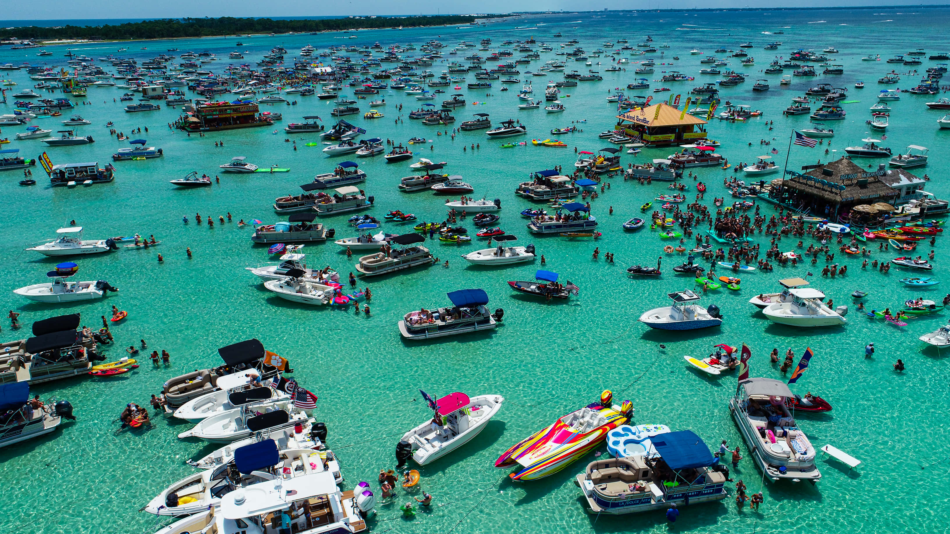 Crab Island 桌布 壁紙 — 俯瞰圖：碧綠海水上擠滿色彩繽紛的船隻和人群，享受熱鬧的海灘派對。