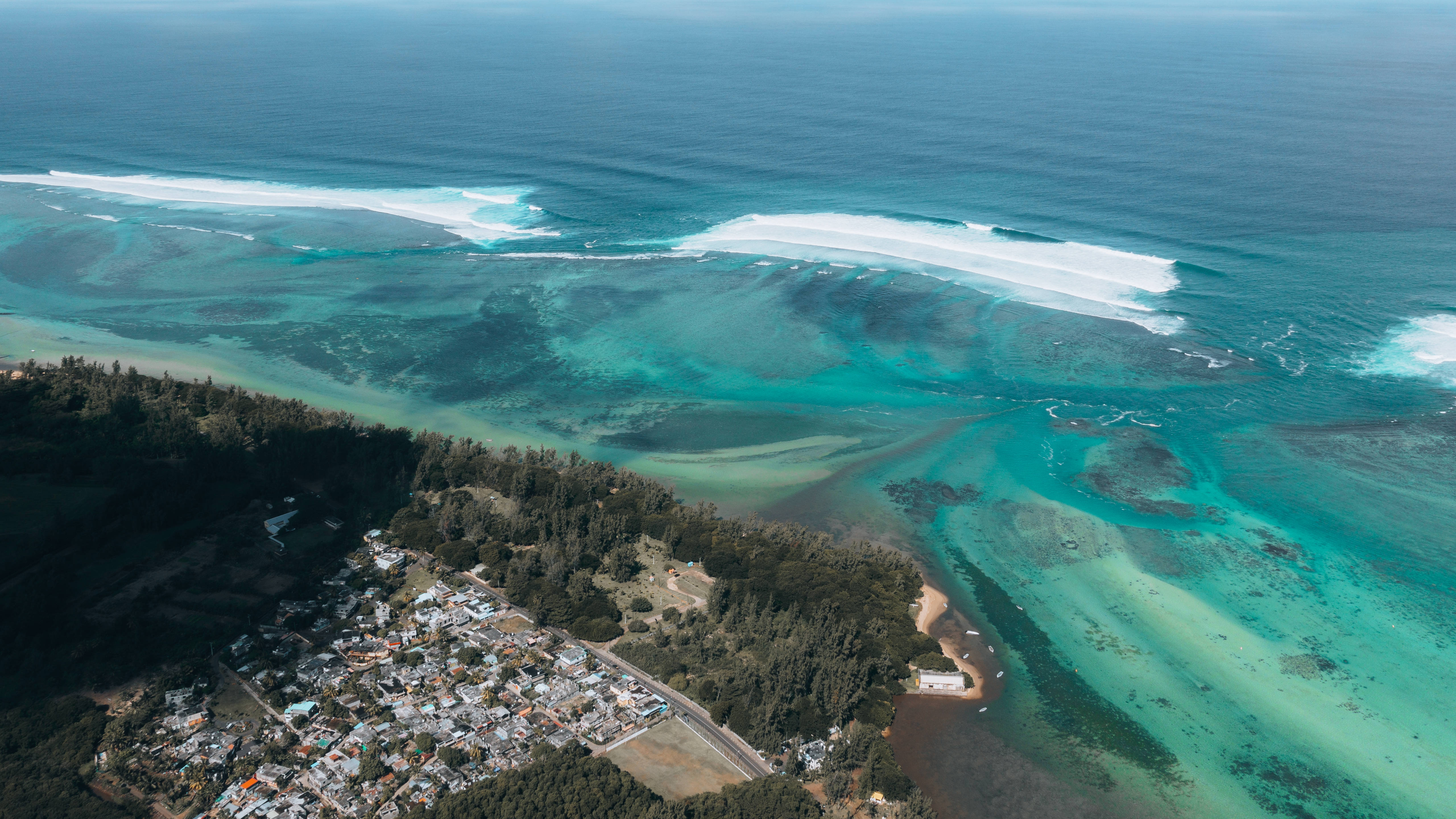 Mauritius 桌布 壁紙 — 俯瞰圖：綠松石色海浪拍打珊瑚礁，旁邊是森林覆蓋的海岸和一個小漁村。