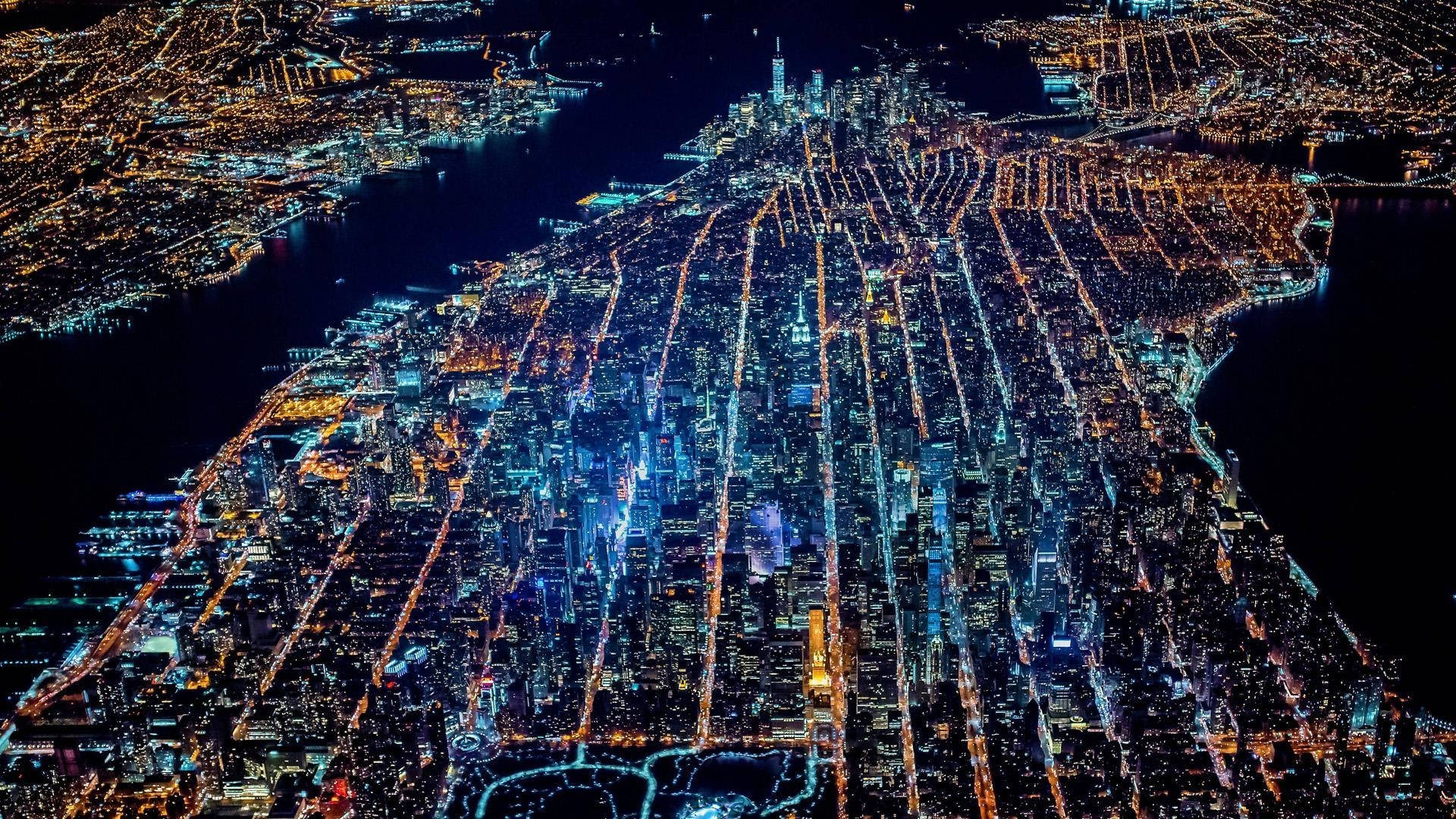 New 桌布 壁紙 — 俯瞰夜景，廣闊的城市景觀沿著網格狀街道閃爍著金色和藍色的燈光。