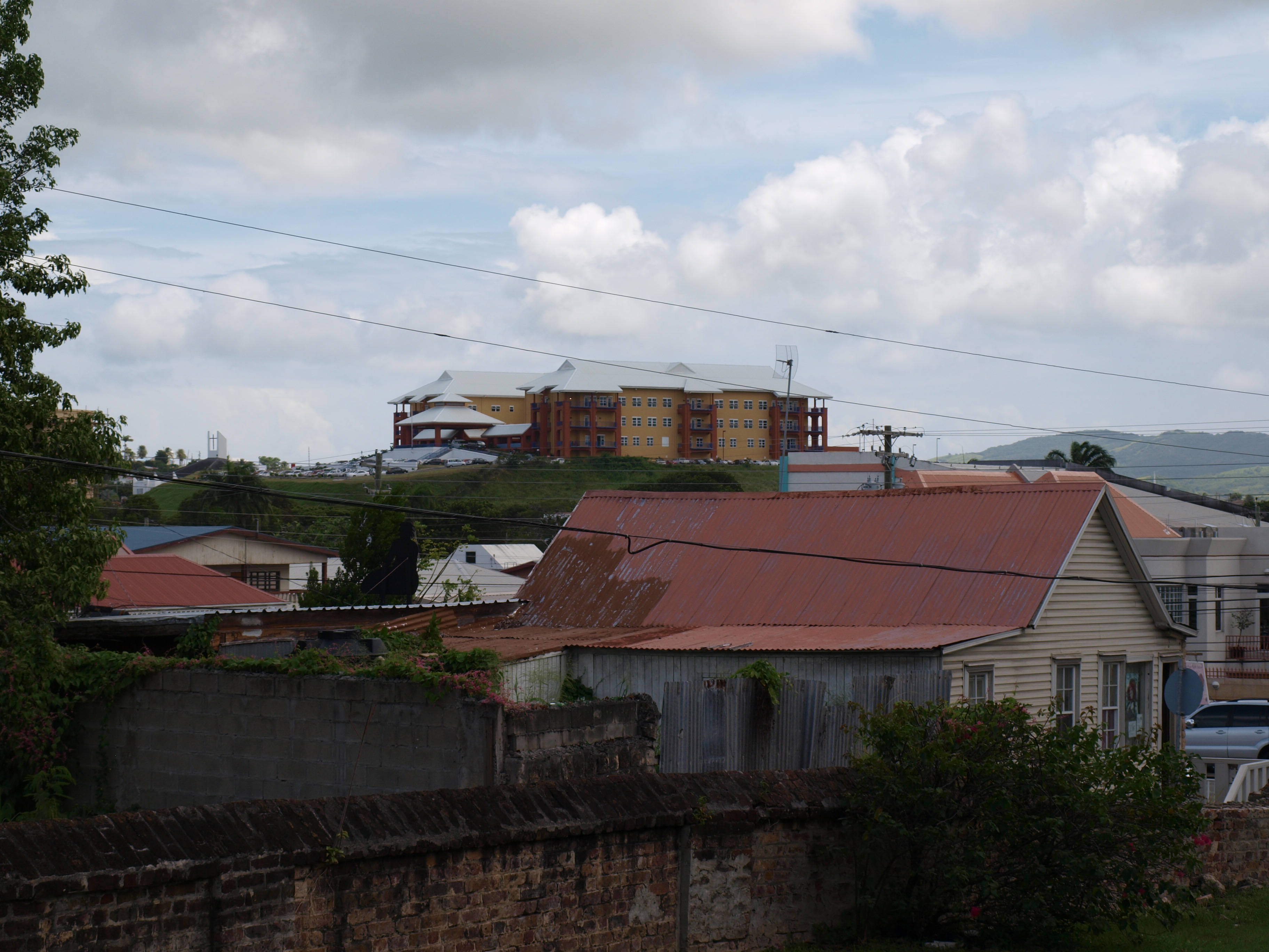Antigua And Barbuda 桌布 壁紙 — 俯瞰山城景觀，有風化的房屋和一座大型現代酒店，天空多雲。