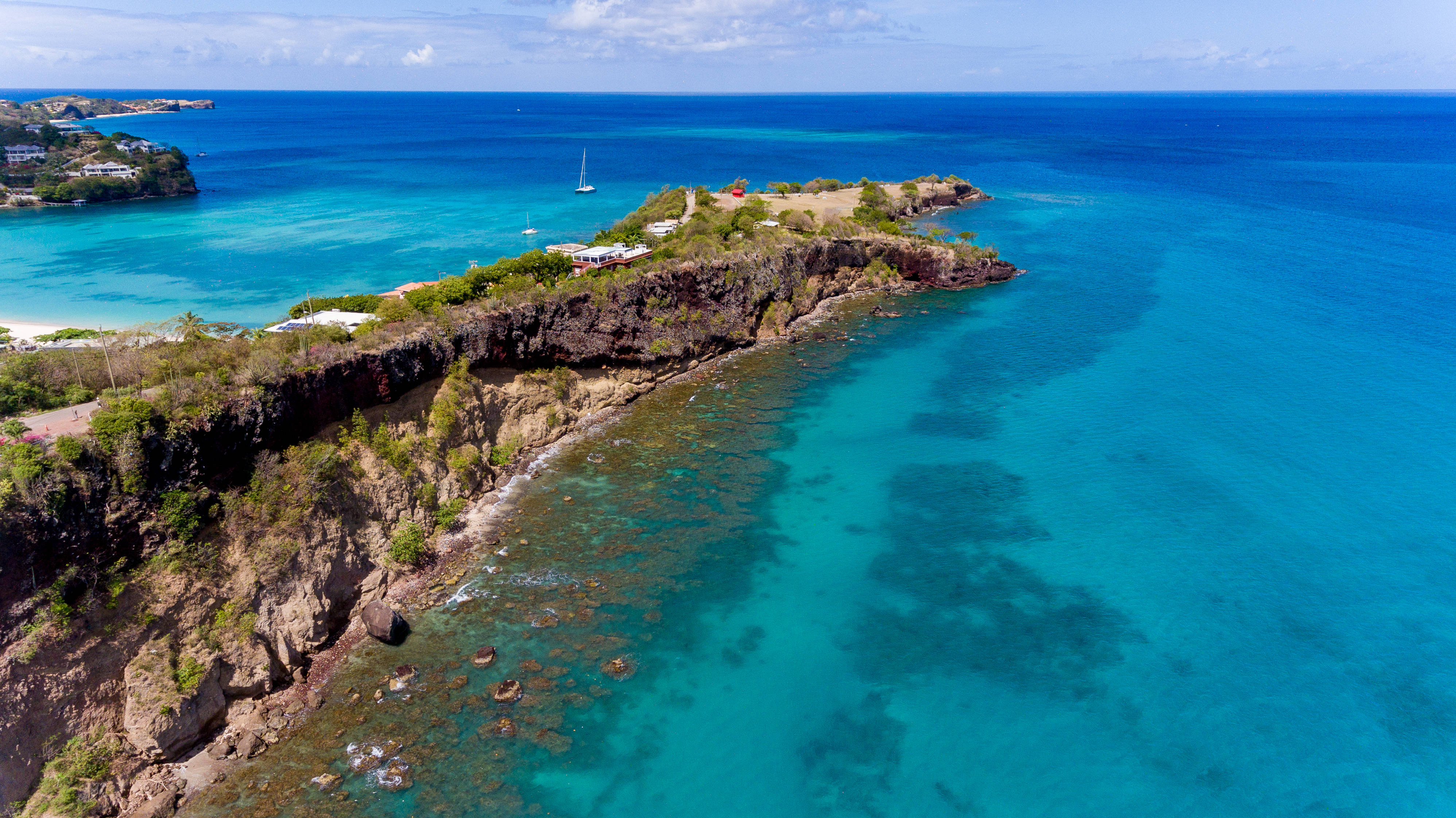 Grenada 桌布 壁紙 — 俯瞰崎嶇懸崖海岸線，碧綠海水，一艘孤帆在明亮藍天下。