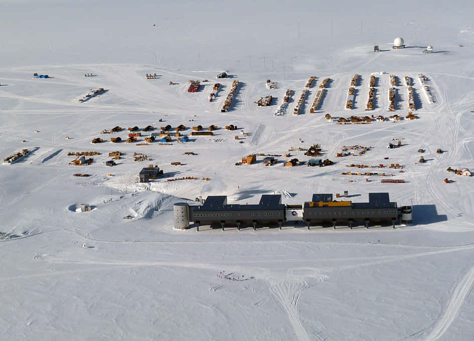 South Pole 桌布 壁紙 — 俯瞰廣闊的南極研究站，模塊化建築和雪地摩托車散落在無盡的白雪中。