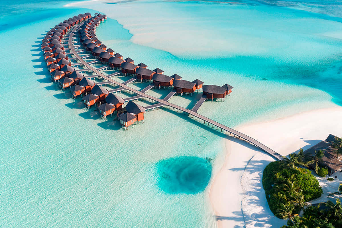 Maldives Island 桌布 壁紙 — 俯瞰彎曲的水上平房度假村，木製步道延伸至碧綠的潟湖水域。