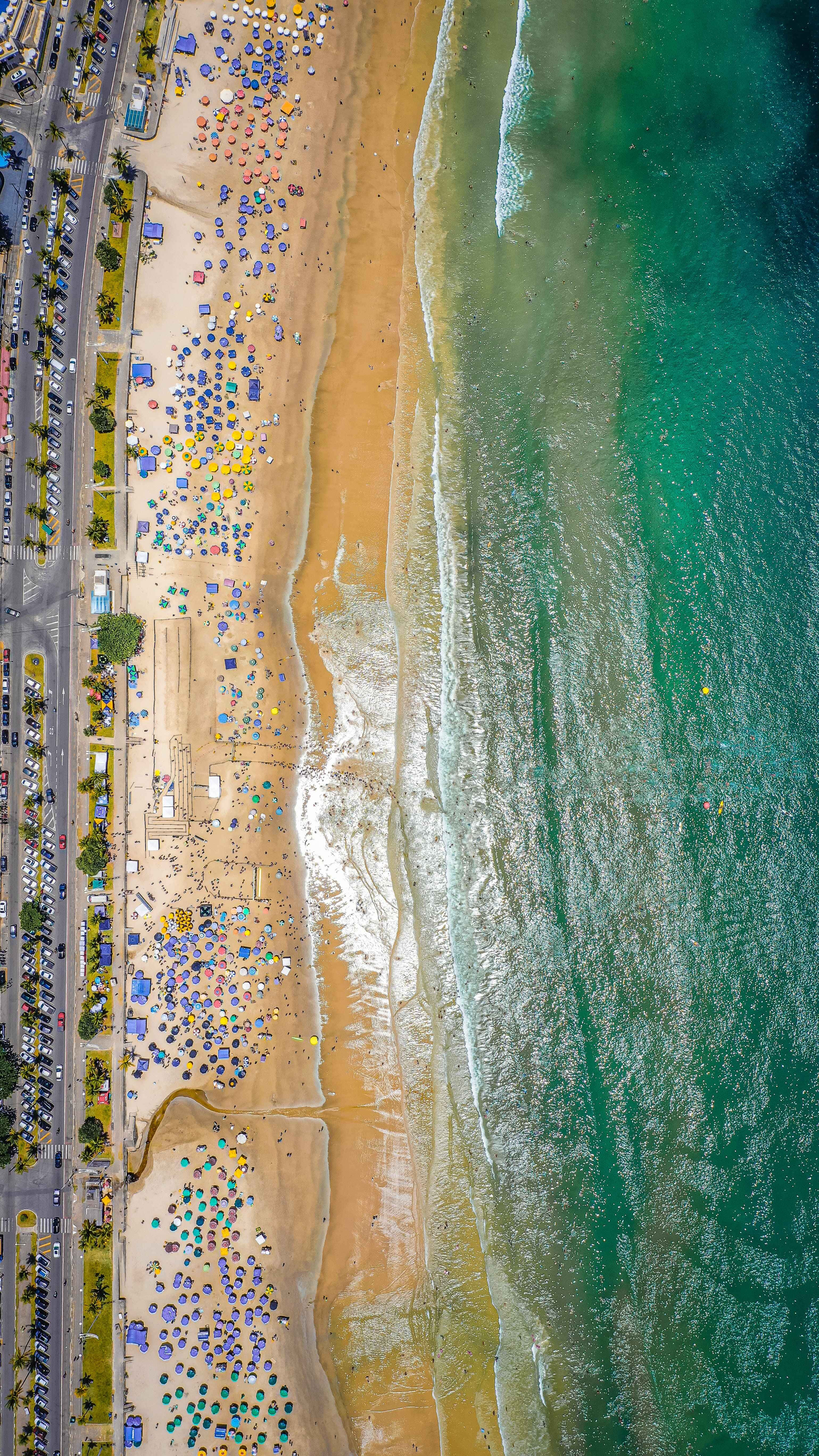 Aesthetic Beachy 桌布 壁紙 — 俯瞰擁擠的海灘，色彩繽紛的遮陽傘點綴在金色沙灘上，旁邊是碧綠的海浪。
