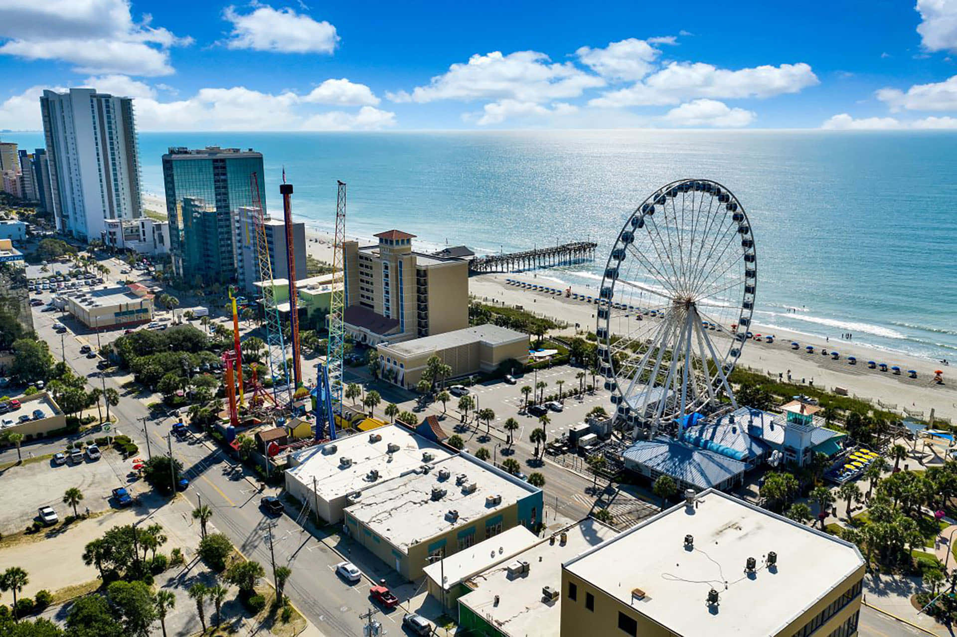 Myrtle Beach 桌布 壁紙 — 俯瞰熱鬧的海濱長廊，巨大的摩天輪聳立在遊樂設施和酒店之上，旁邊是碧綠的海浪。