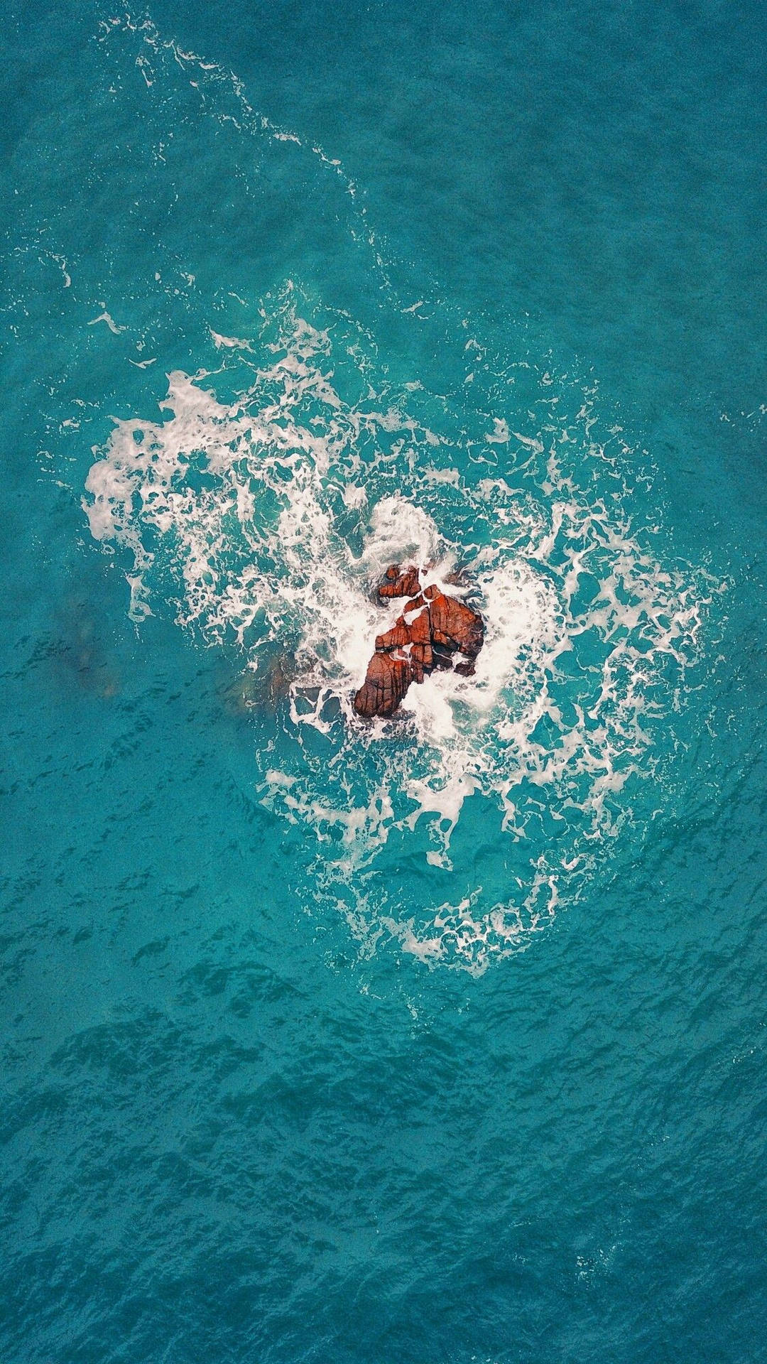 俯瞰碧綠海洋波浪拍打崎嶇岩層的航拍景象。