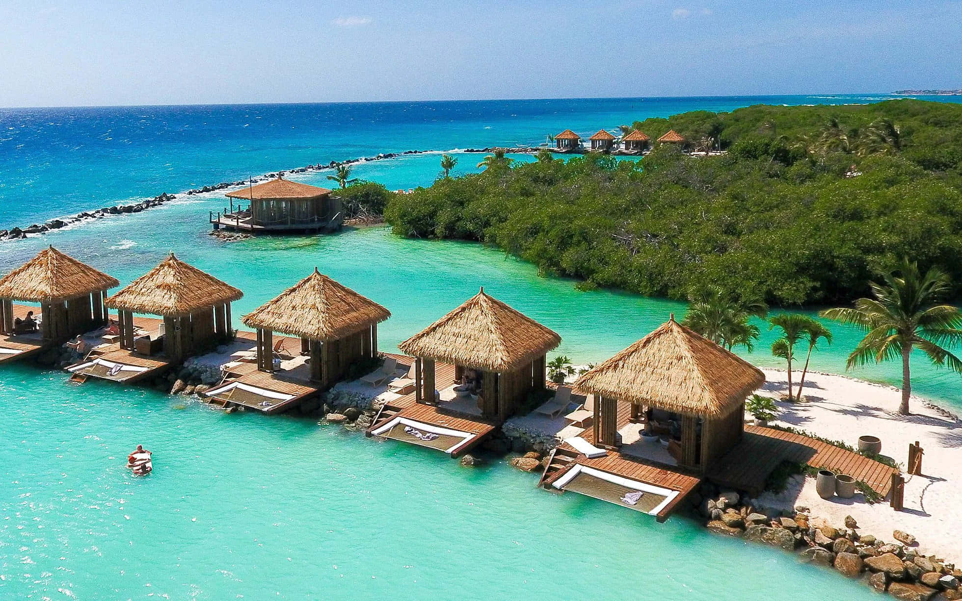Aruba 桌布 壁紙 — 俯瞰茅草屋頂水上平房，坐落在碧綠海水旁，毗鄰鬱鬱蔥蔥的綠色島嶼。