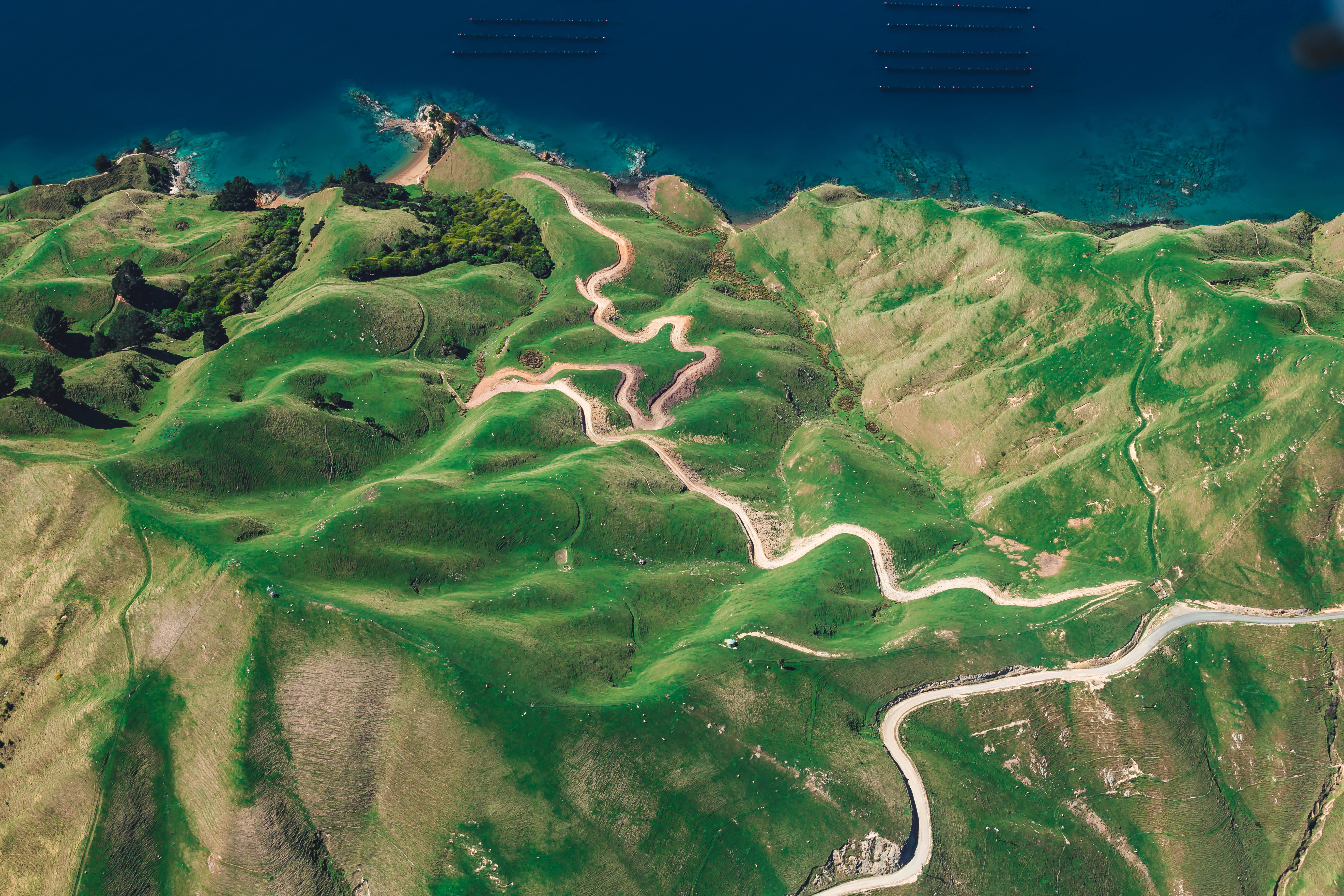 桌面 4K 桌布 壁紙 — 俯瞰蜿蜒的沿海公路穿過鬱鬱蔥蔥的綠色山丘，與深藍色的海洋交匯。