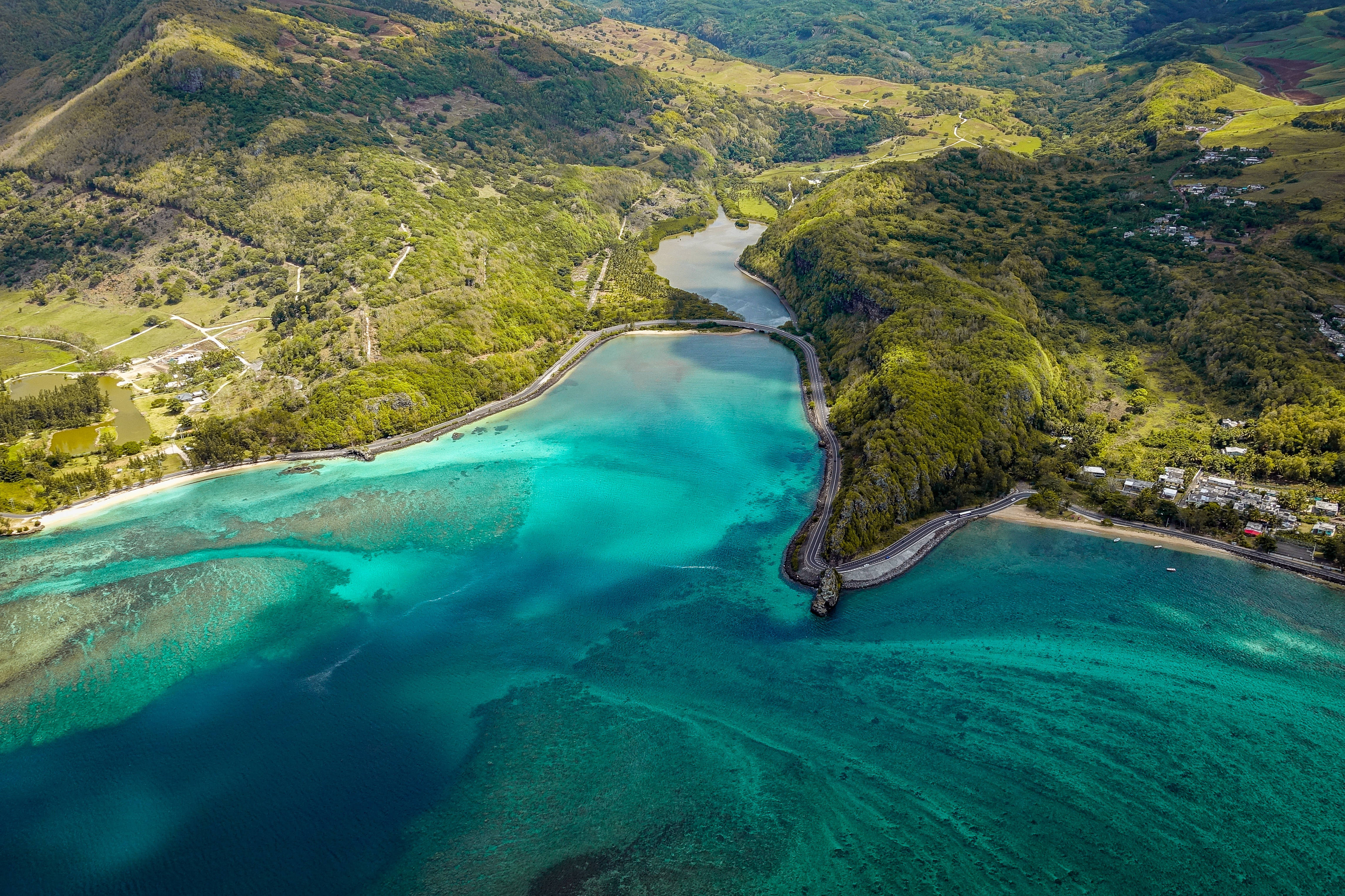 Mauritius 桌布 壁紙 — 俯瞰蜿蜒的藍綠色潟湖，周圍環繞著鬱鬱蔥蔥的綠色山丘，沿海道路和散落的建築物。