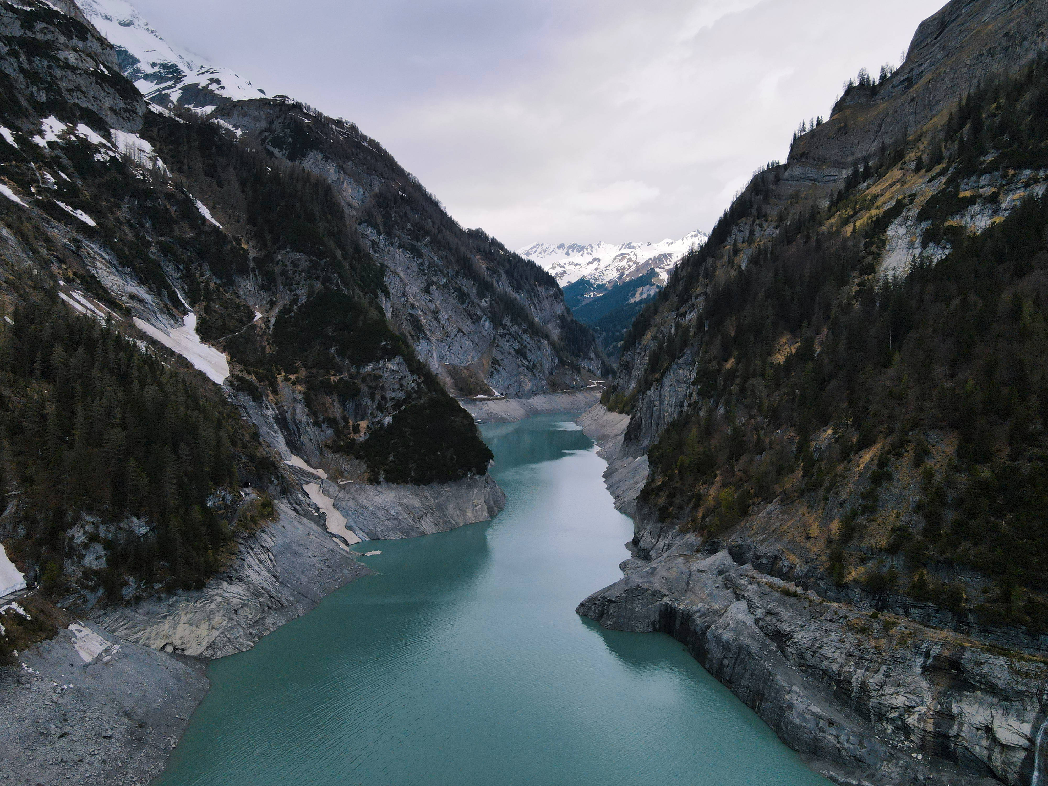 Topography 桌布 壁紙 — 俯瞰視角，一個藍綠色冰川湖坐落於積雪覆蓋的山脈之間，天空多雲。