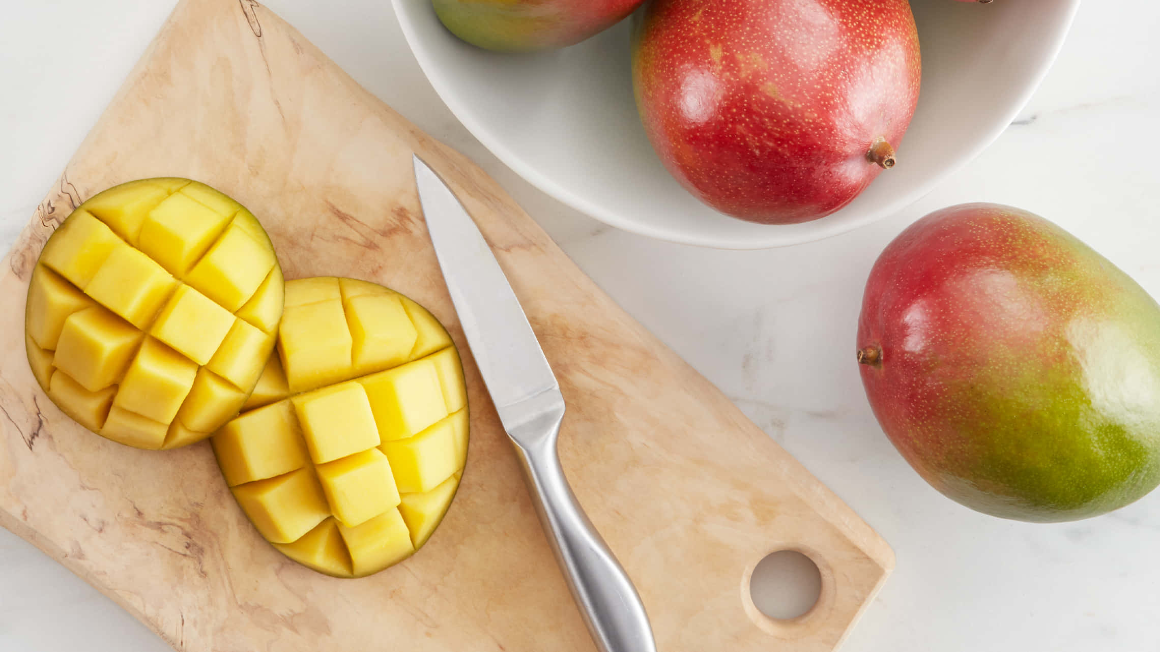 Mango 桌布 壁紙 — 俯瞰鏡頭下，多汁芒果片在木砧板上劃出網格，旁邊有刀和碗中的完整芒果。
