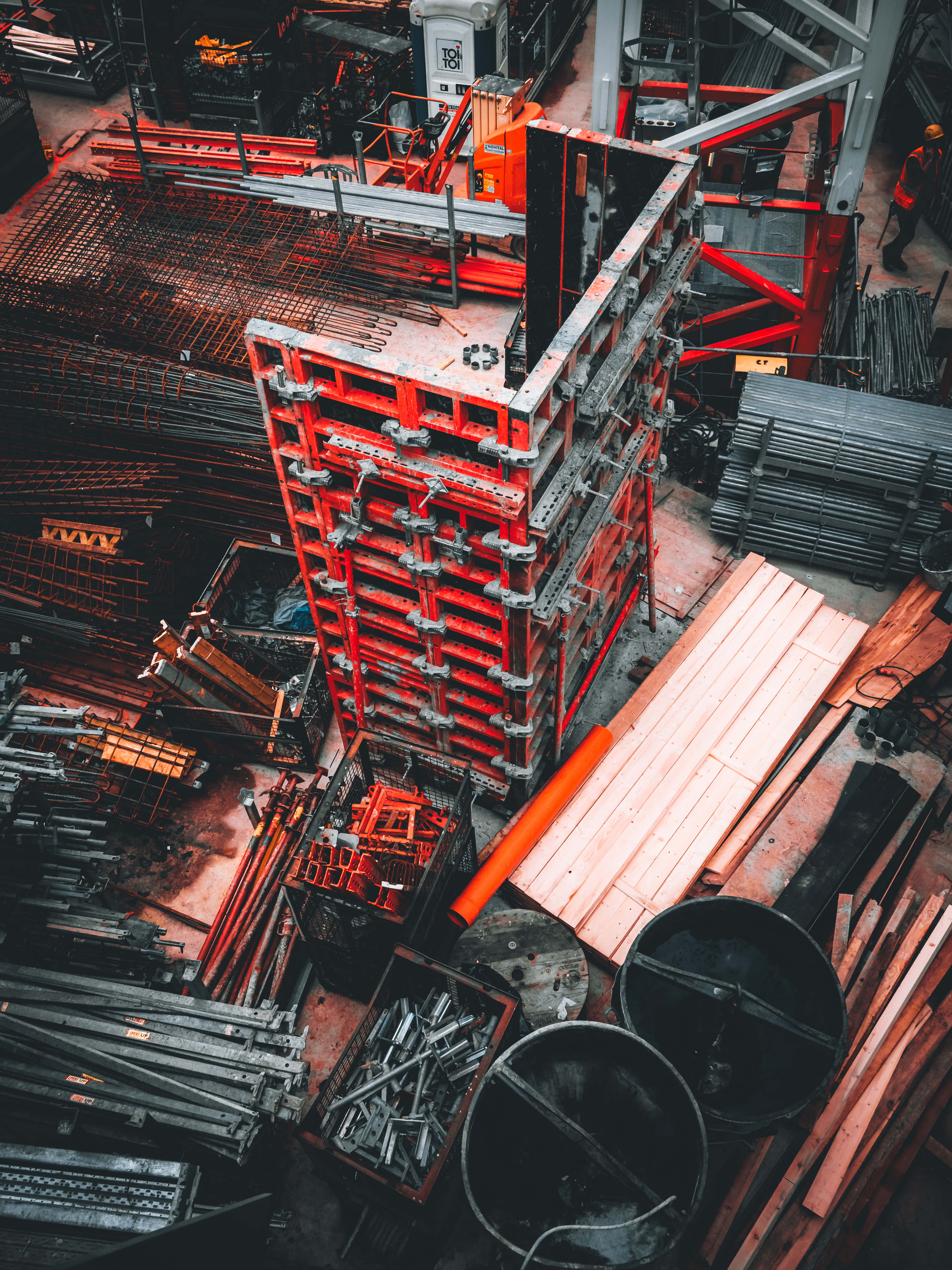 Civil Engineering 桌布 壁紙 — 俯瞰雜亂的建築工地，紅色金屬鷹架聳立在鋼筋和木板堆之上。