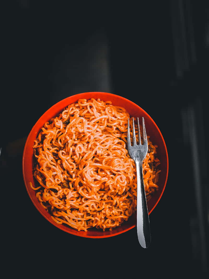 Food Photography 桌布 壁紙 — 俯視一個充滿蒸氣即食麵和銀色叉子的鮮橙色碗，背景為深色。