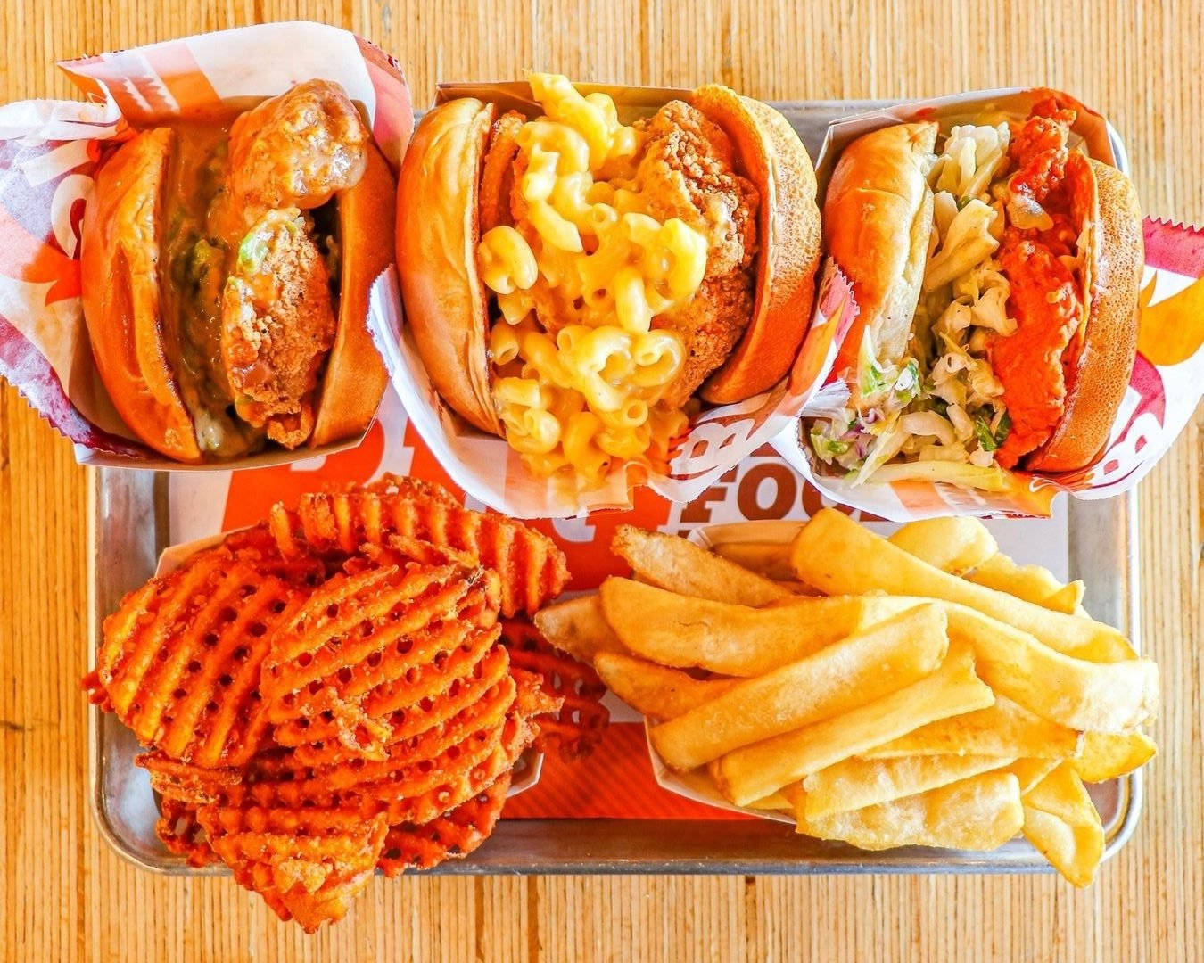 French Fries 桌布 壁紙 — 俯視一個托盤，上面有三個餡料豐富的三明治，以及格子薯條和普通薯條作為配菜，放在木桌上。