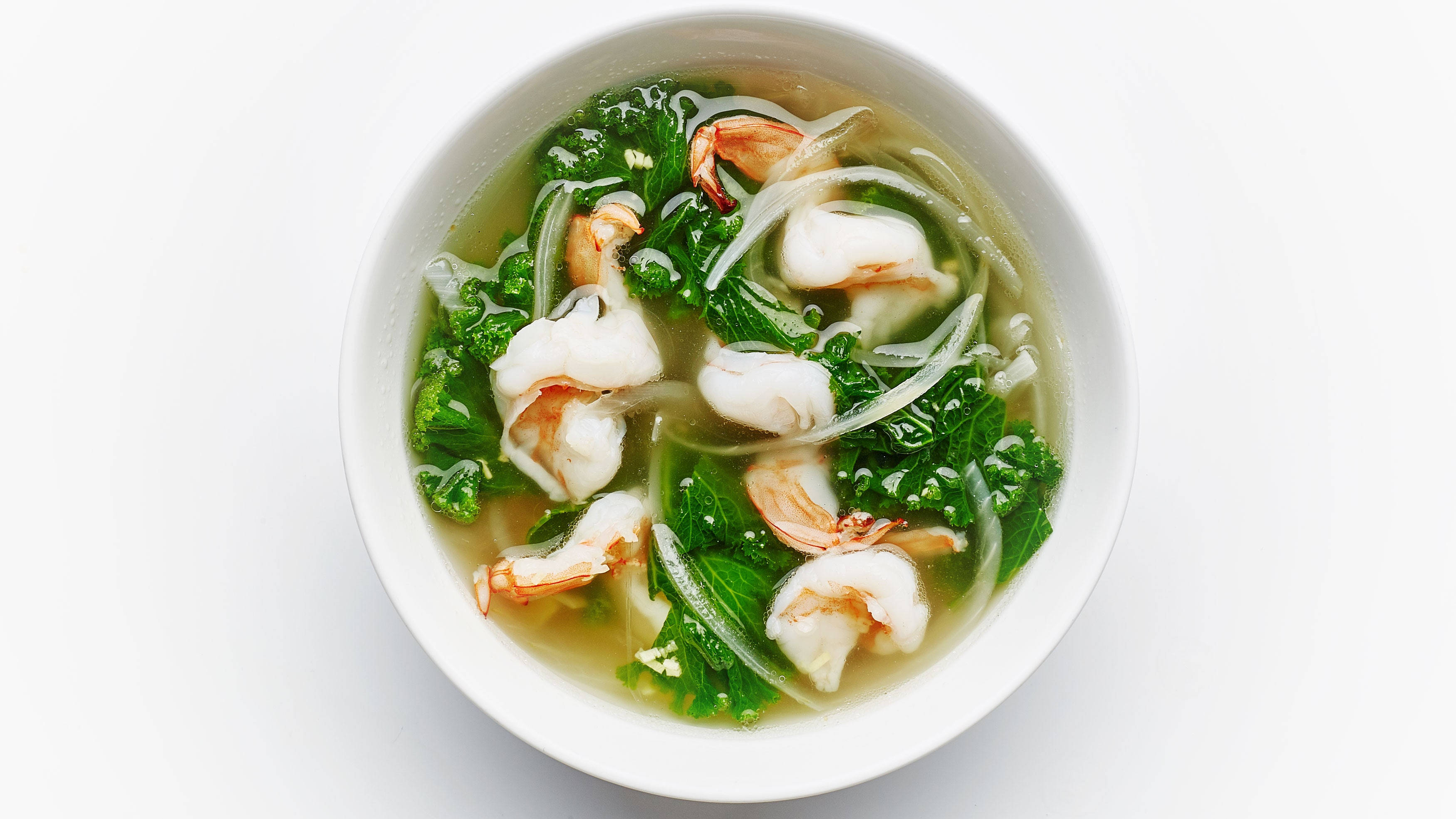 shrimp 桌布 壁紙 — 俯視一個白色碗，裡面裝滿清澈湯底、蝦、羽衣甘藍和麵條，背景為純白色。