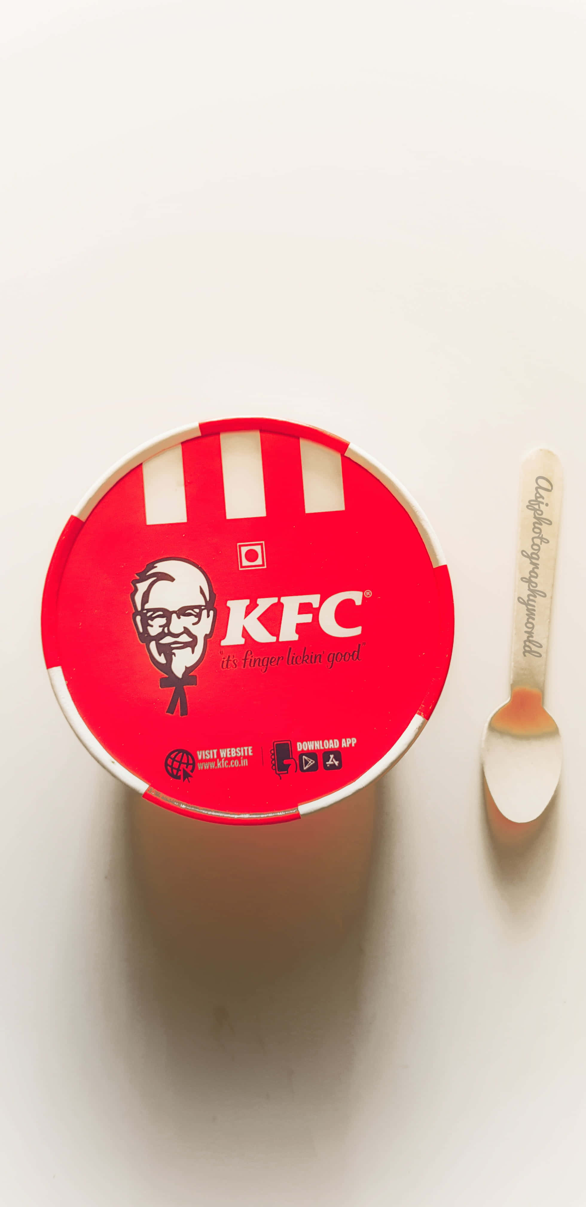 Kfc 桌布 壁紙 — 俯視圖：一個紅色KFC桶，旁邊放著一隻品牌湯匙，置於純白表面上。