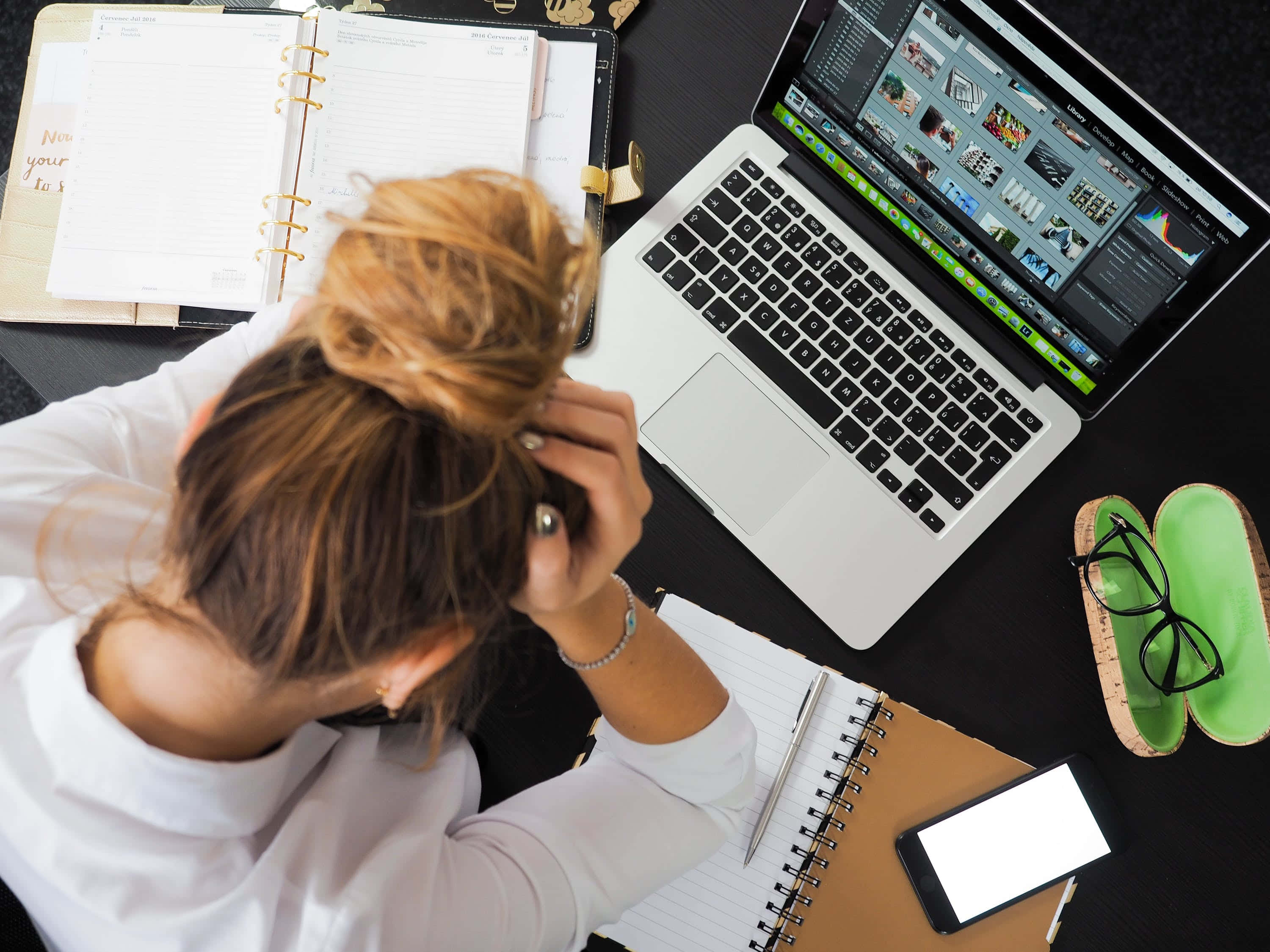 MacBook 動態圖片 桌布 壁紙 — 俯視圖，一名金髮盤髻的女性，在雜亂的辦公桌上使用筆記型電腦、筆記本和電話，感到壓力。