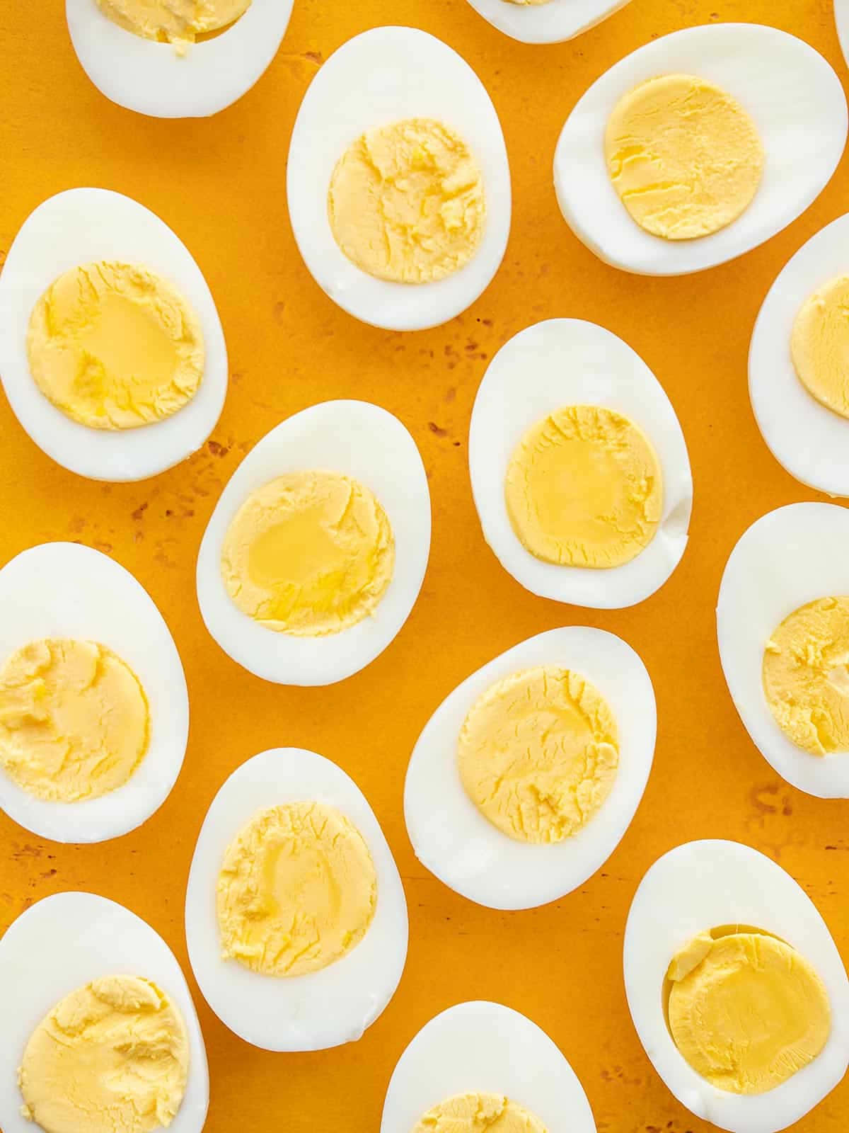 Eggs 桌布 壁紙 — 俯視圖：半邊水煮蛋搭配奶油狀蛋黃，整齊排列在鮮豔的橙色表面上。