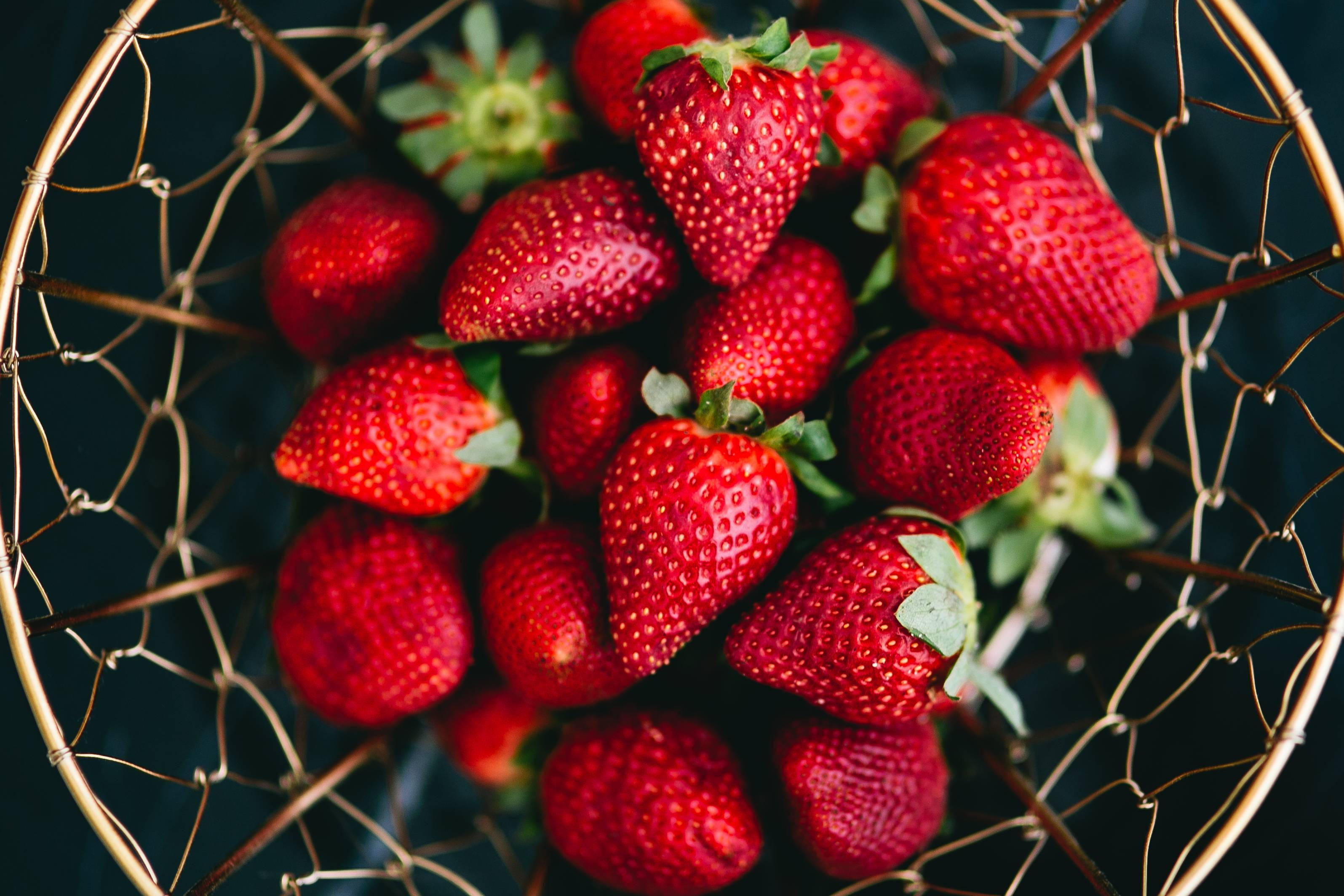 Fruit 桌布 壁紙 — 俯視圖，深色背景上，一個金色鐵絲籃裡裝滿了飽滿的紅草莓，帶有綠色蒂頭。