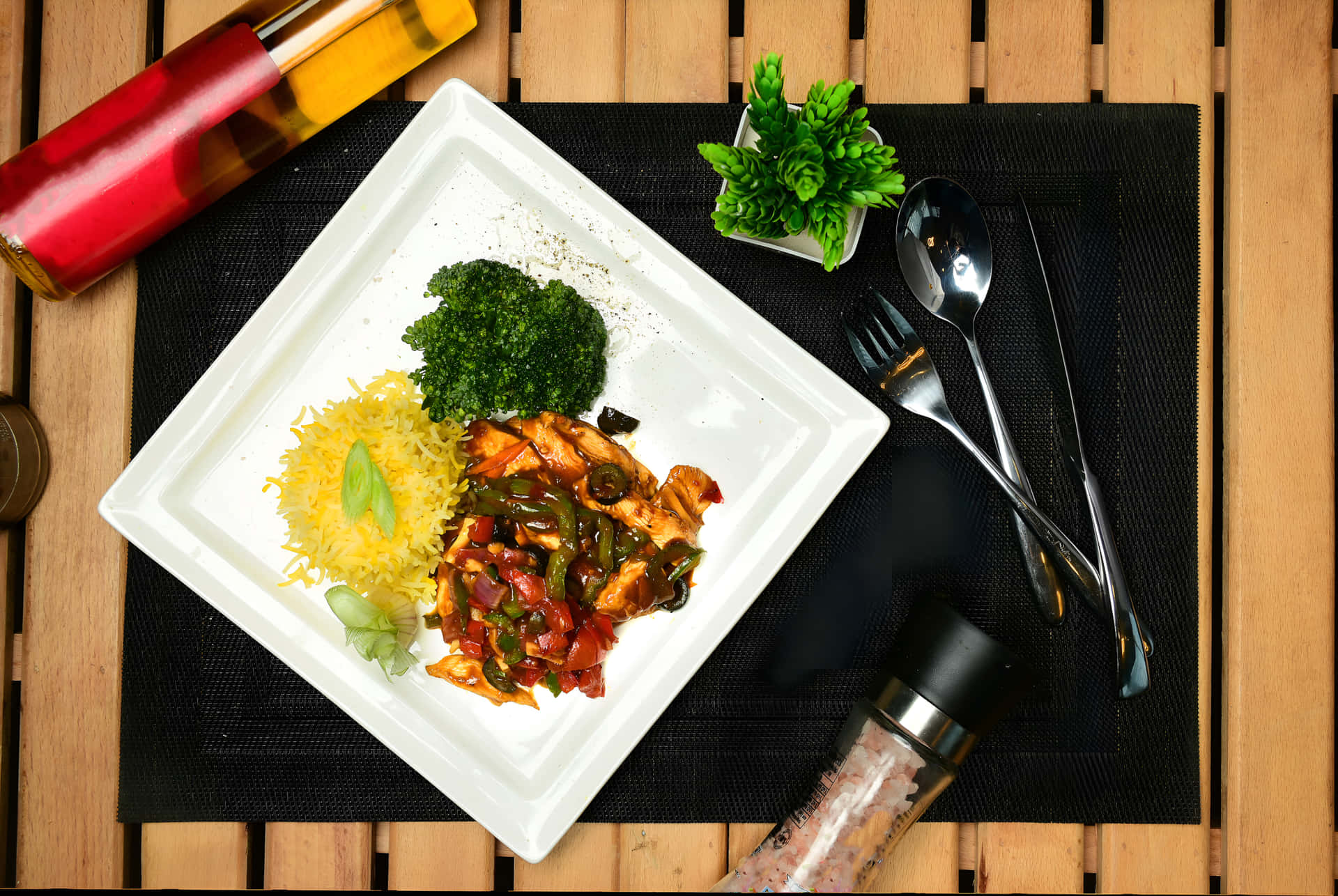 Chicken Chilli Dry with rice on a plate 壁紙 — 俯視圖：白色盤子盛裝雞肉炒花椰菜和黃薑飯，放在黑色墊子上，附近有餐具和瓶子。