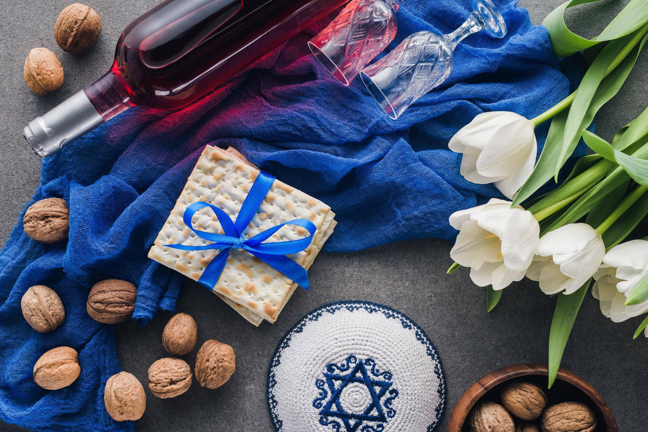 Passover 桌布 壁紙 — 俯視圖展示逾越節家宴物品，包括無酵餅、葡萄酒、鬱金香和基帕，排列在藍色布料上。