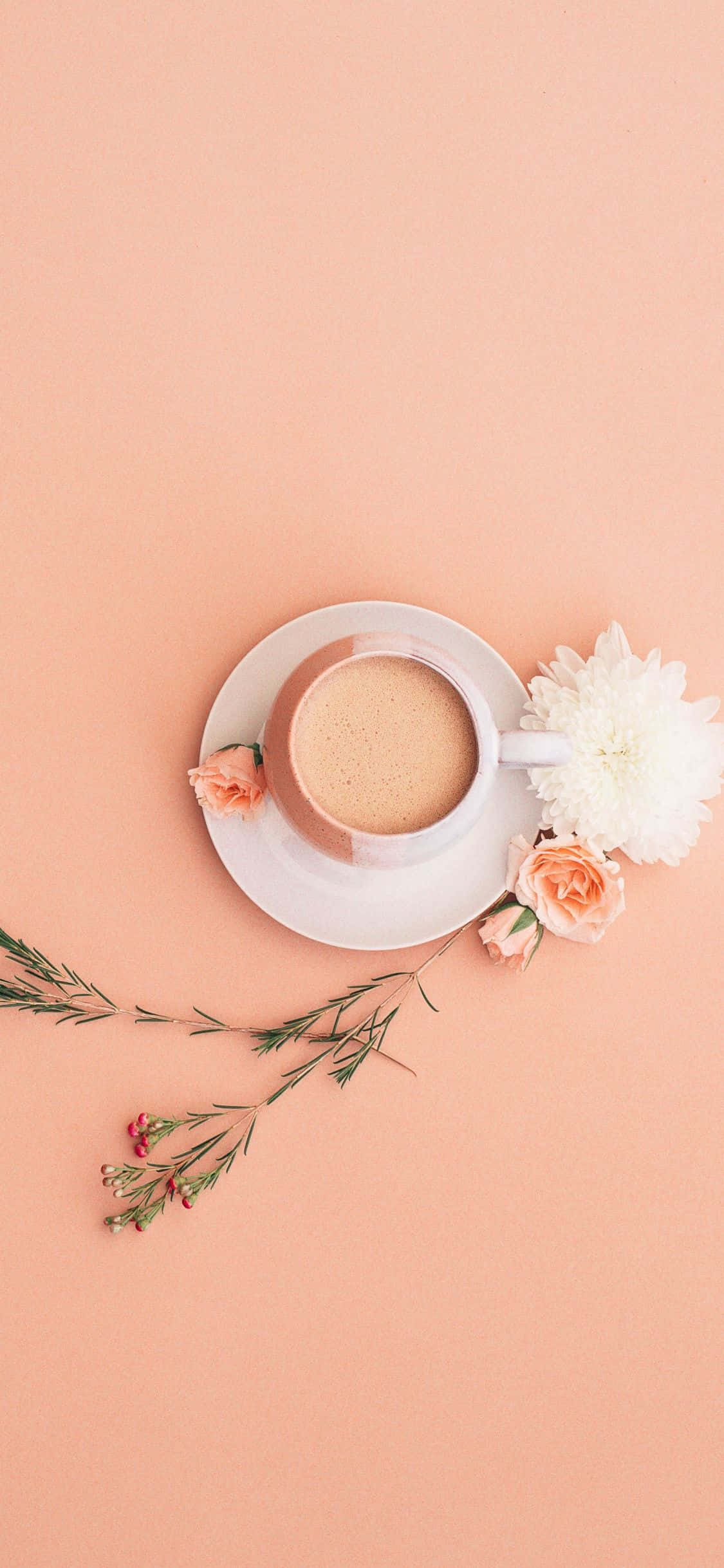 Minimalist Flower Computer 桌布 壁紙 — 俯視角度下，一個放在碟子上的咖啡杯，被花朵和綠色植物環繞，背景是柔和蜜桃色。