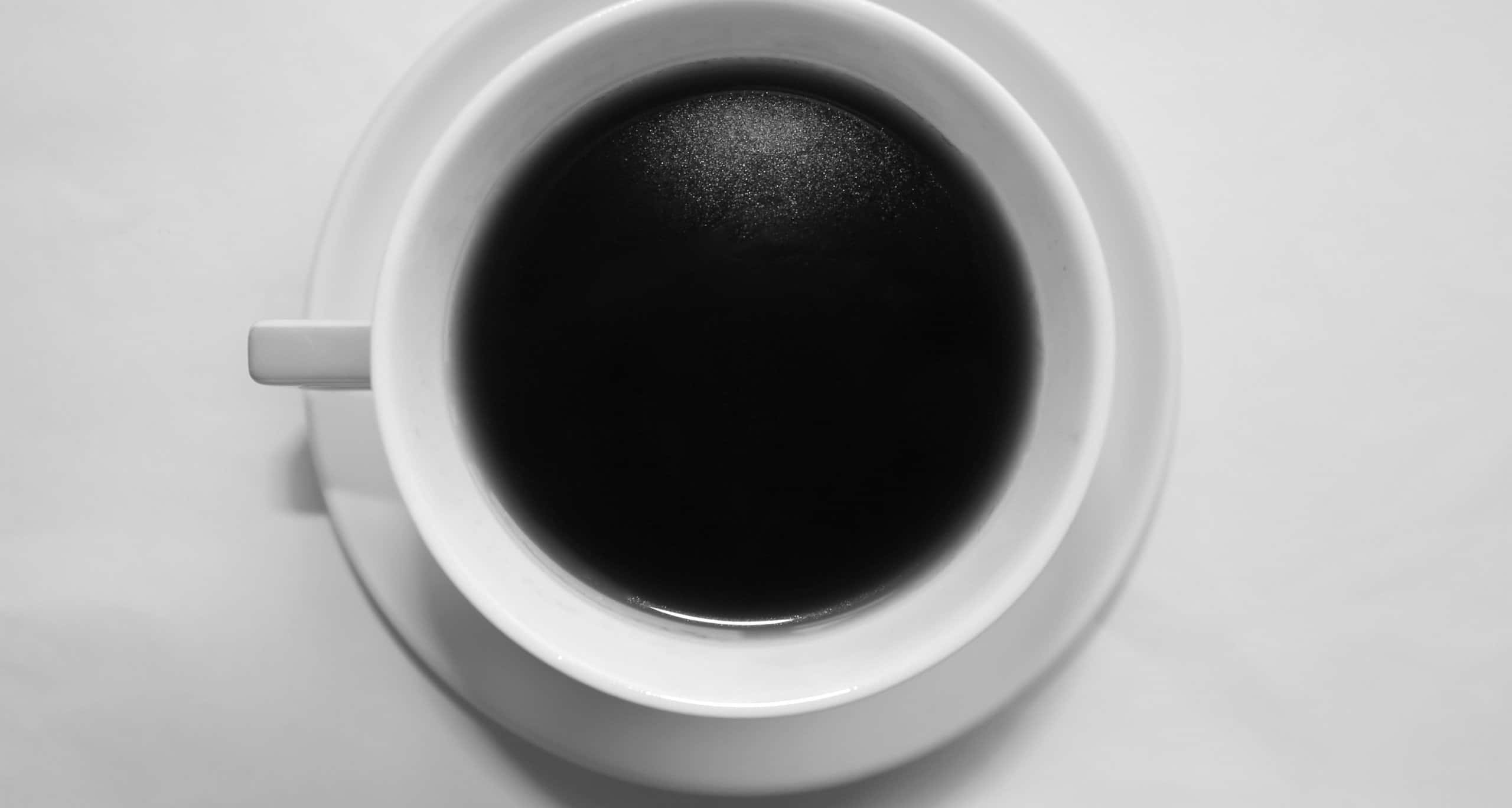 Black Coffee 桌布 壁紙 — 俯視角度下，一個白色陶瓷杯盛滿黑咖啡，放在相配的碟子上，背景為純色淺色。