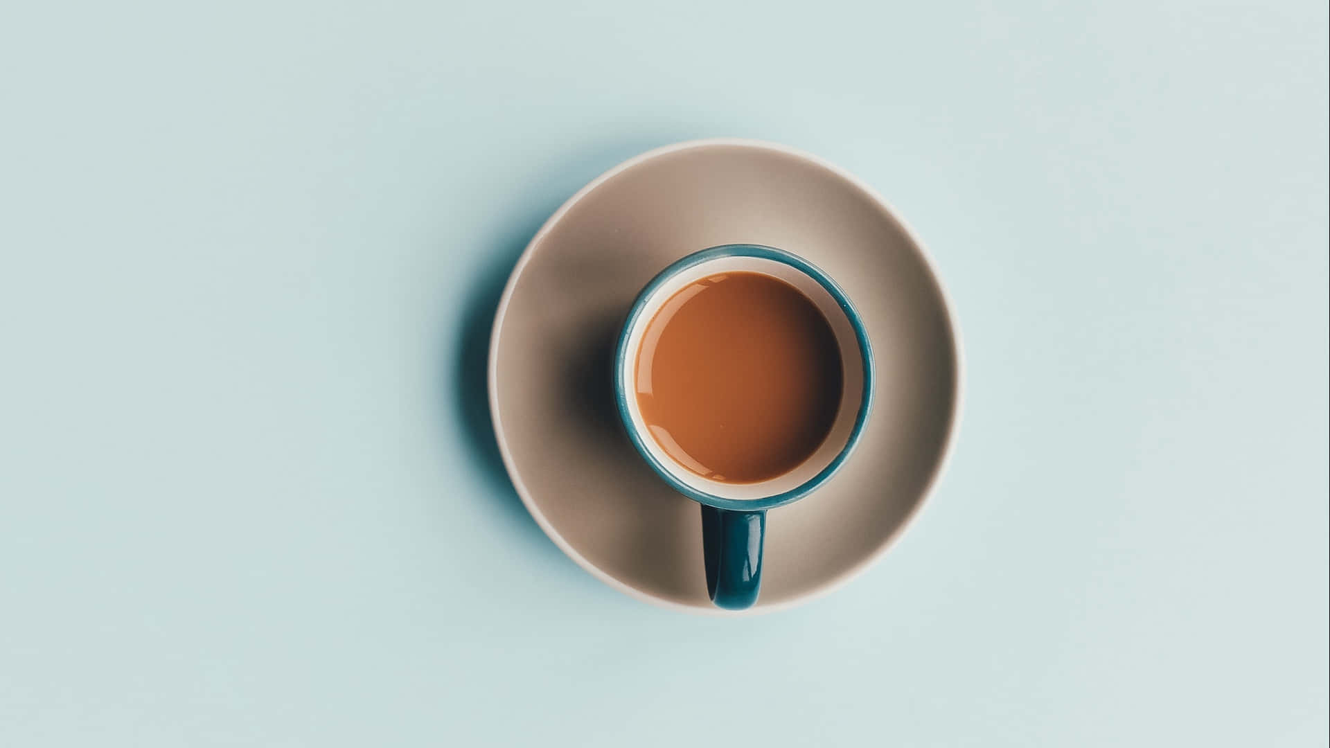 Minimalist Coffee 桌布 壁紙 — 俯視角度下，一個裝有棕色液體的青綠色邊緣咖啡杯，放在米色碟子上，背景為柔和藍色。