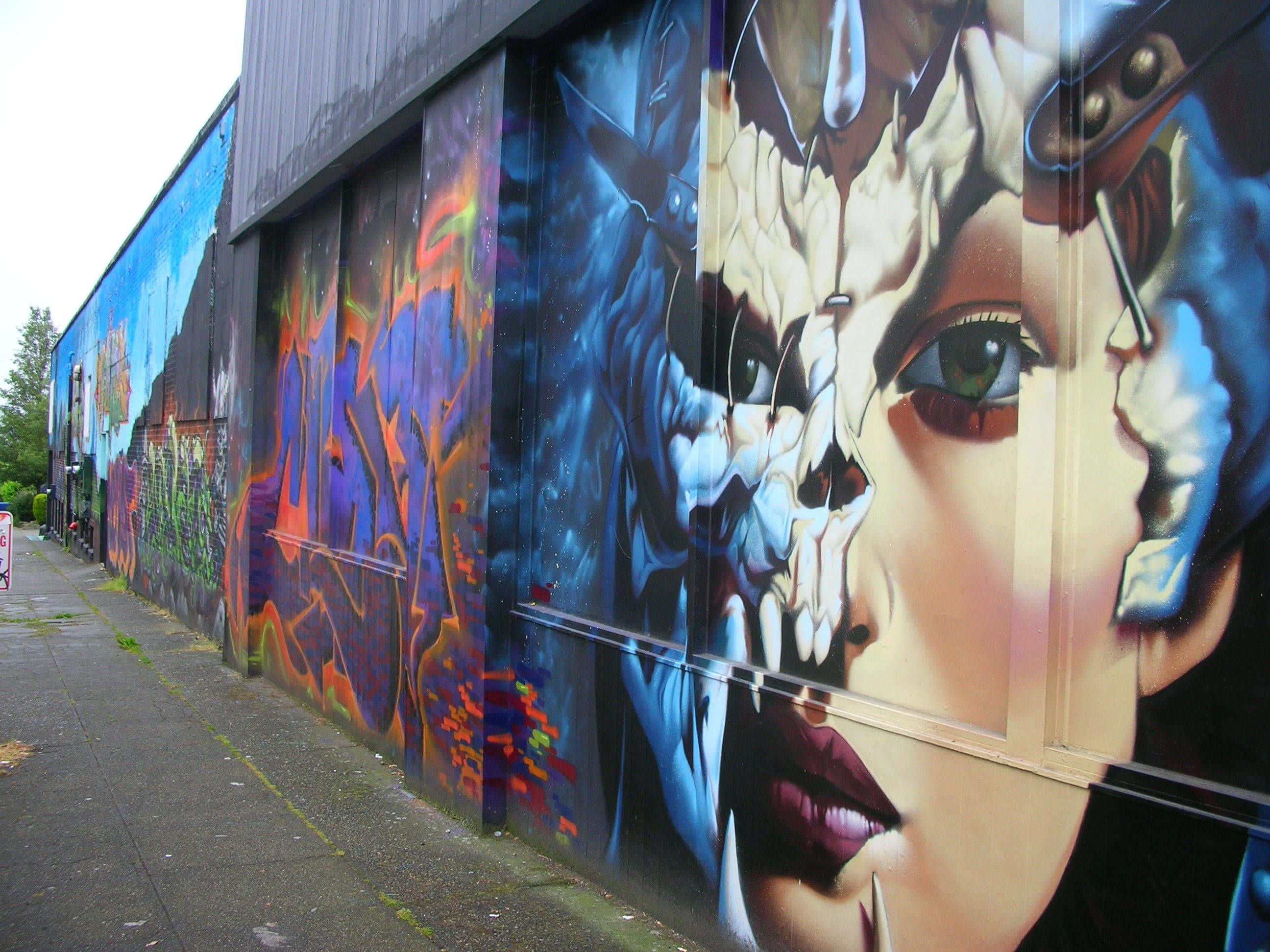 Graffiti Art 桌布 壁紙 — 倉庫牆上充滿活力的塗鴉壁畫，呈現女性面孔與頭骨及宇宙元素的超現實融合。