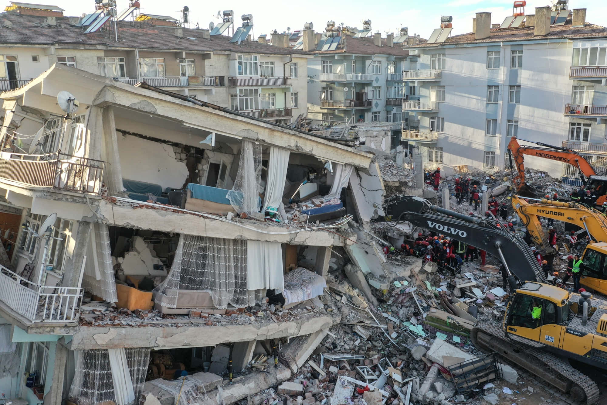 Earthquake 桌布 壁紙 — 倒塌的公寓大樓，內部暴露，救援隊在瓦礫中使用挖掘機。