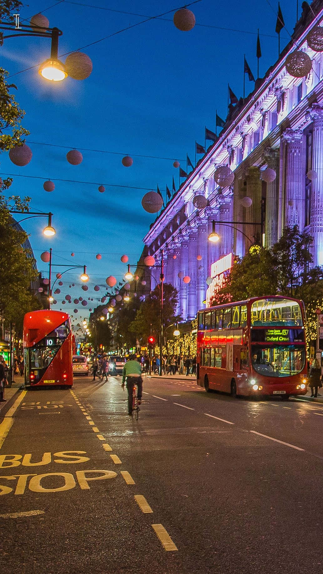London iPhone 桌布 壁紙 — 倫敦充滿活力的傍晚街景，紅色雙層巴士和閃爍的節日燈飾映襯著深藍色的天空。