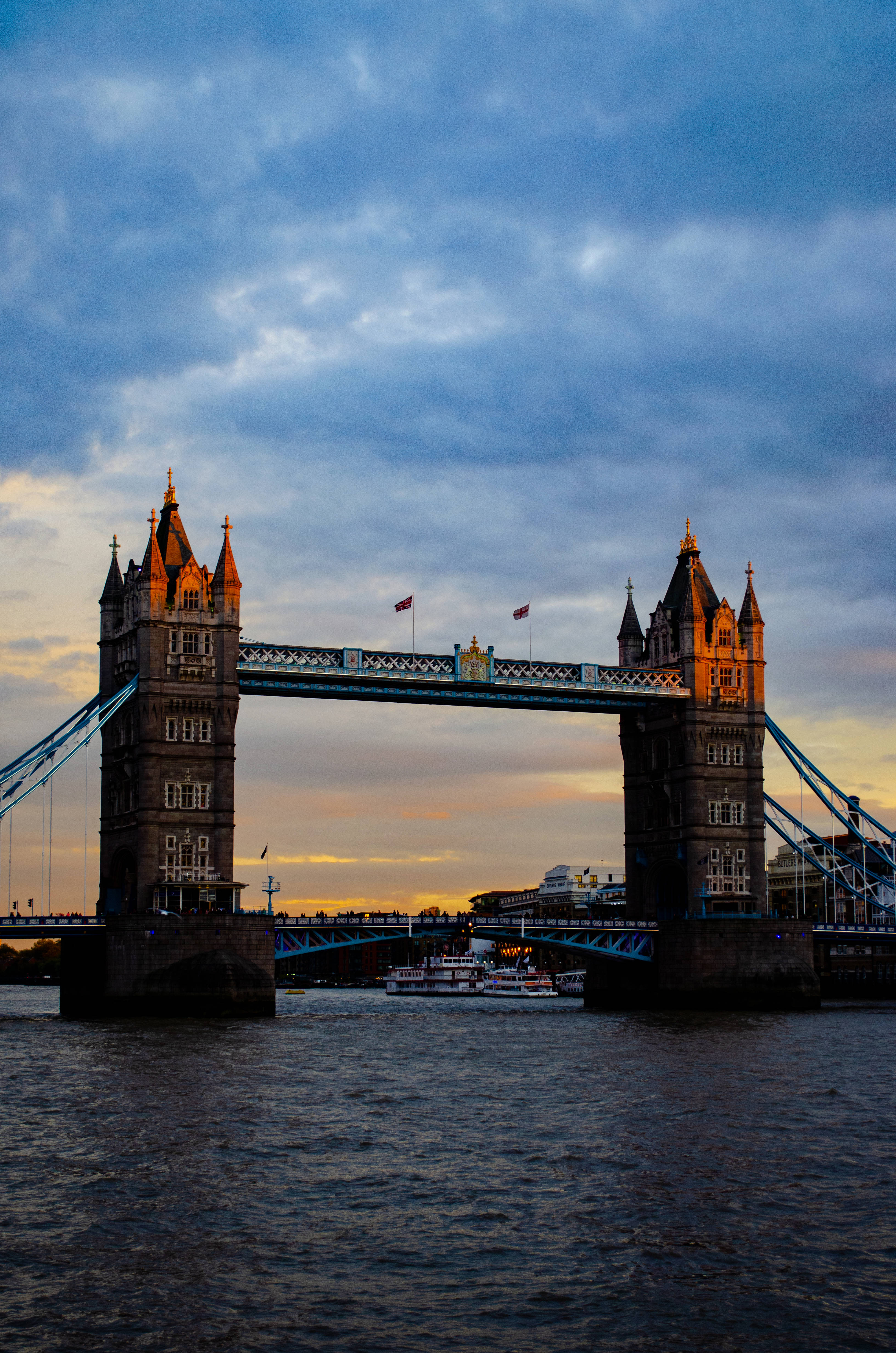 bridge 桌布 壁紙 — 倫敦塔橋在戲劇性的暮色天空下溫暖地發光，船隻在其標誌性塔樓下滑行。